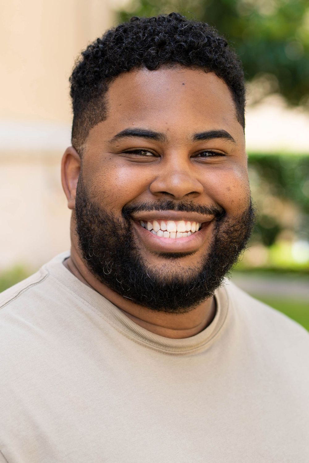Cheerful person with full beard wearing beige t-shirt in outdoor portrait. Portrava Creative Studios