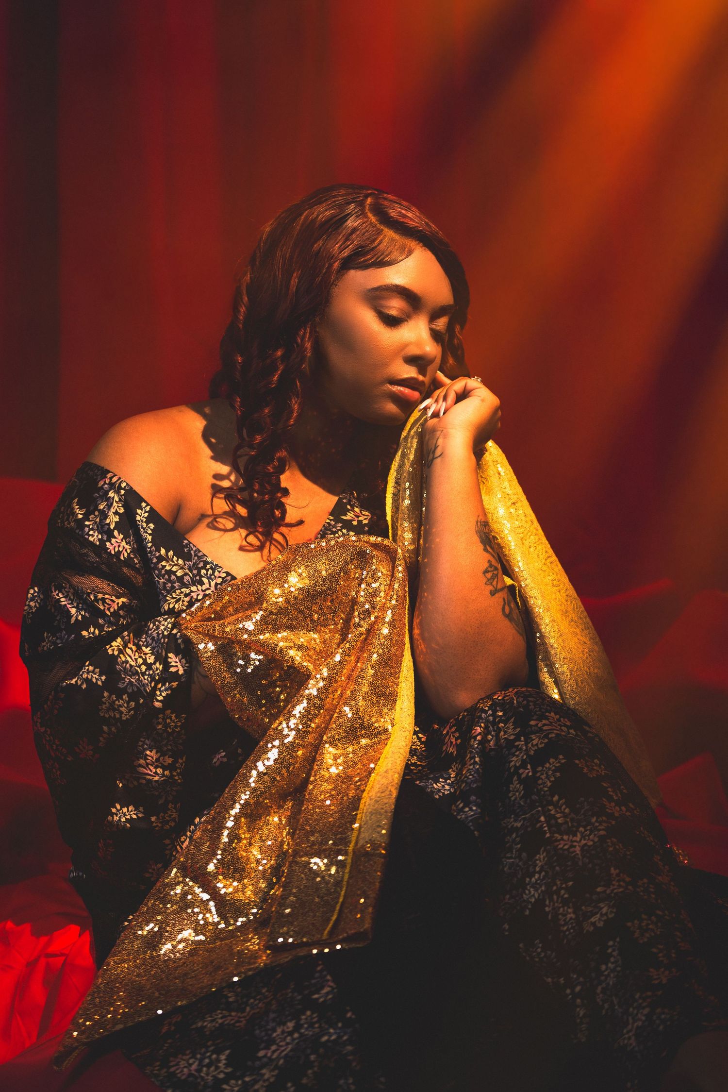 Fashion model in black lace and gold dress poses dramatically against red dramatic lighting. Portrava Creative Studios