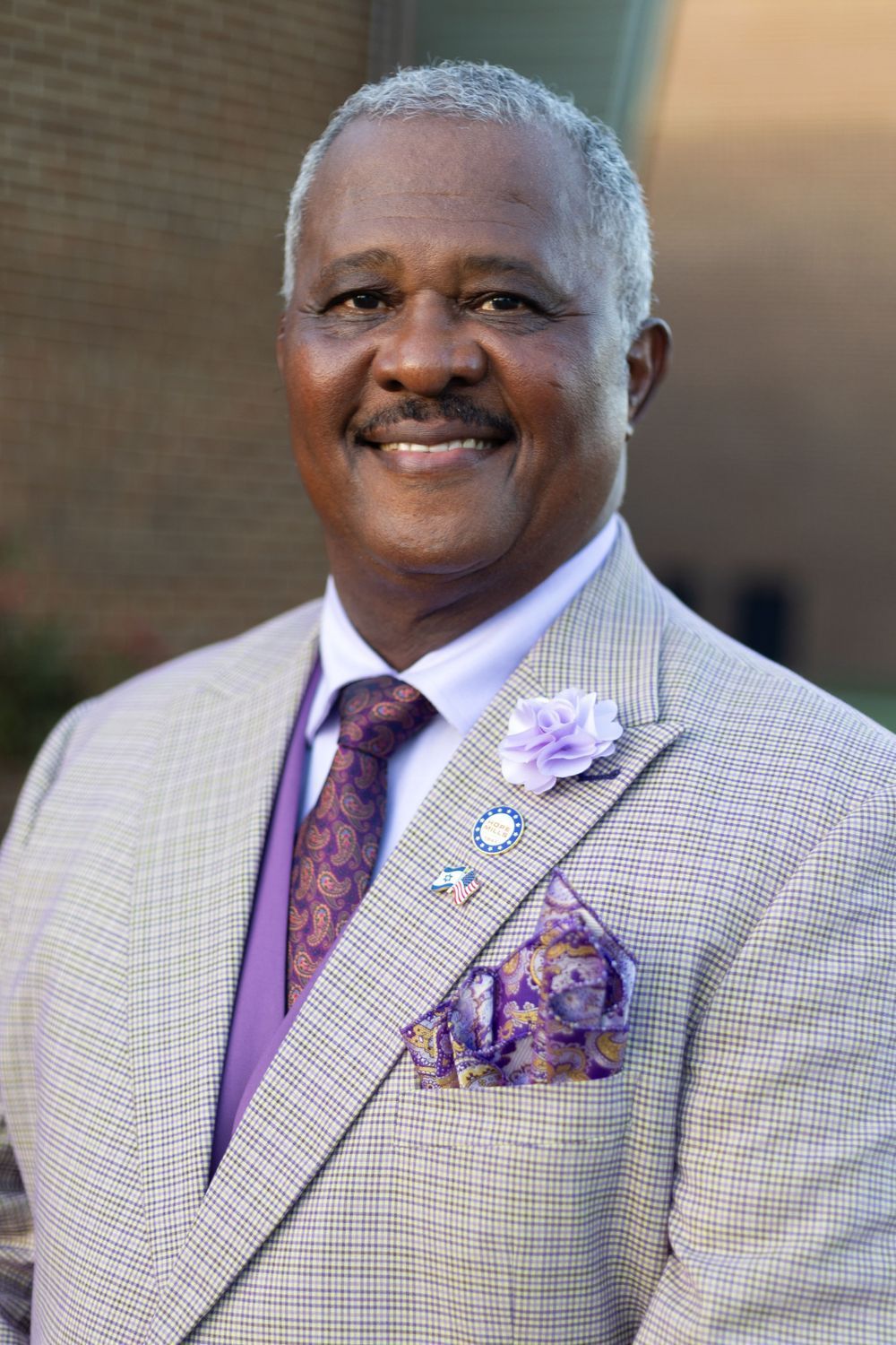 Professional headshot of person wearing a light checkered suit jacket with purple tie and pocket square. Portrava Creative Studios