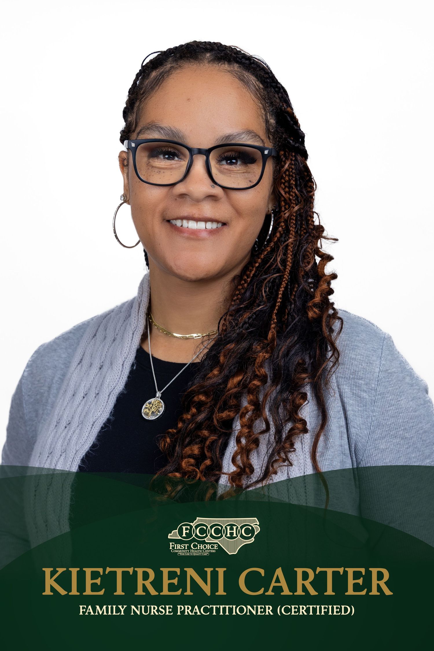 Professional headshot of a healthcare worker wearing glasses and a grey sweater with a warm smile against a dark background.