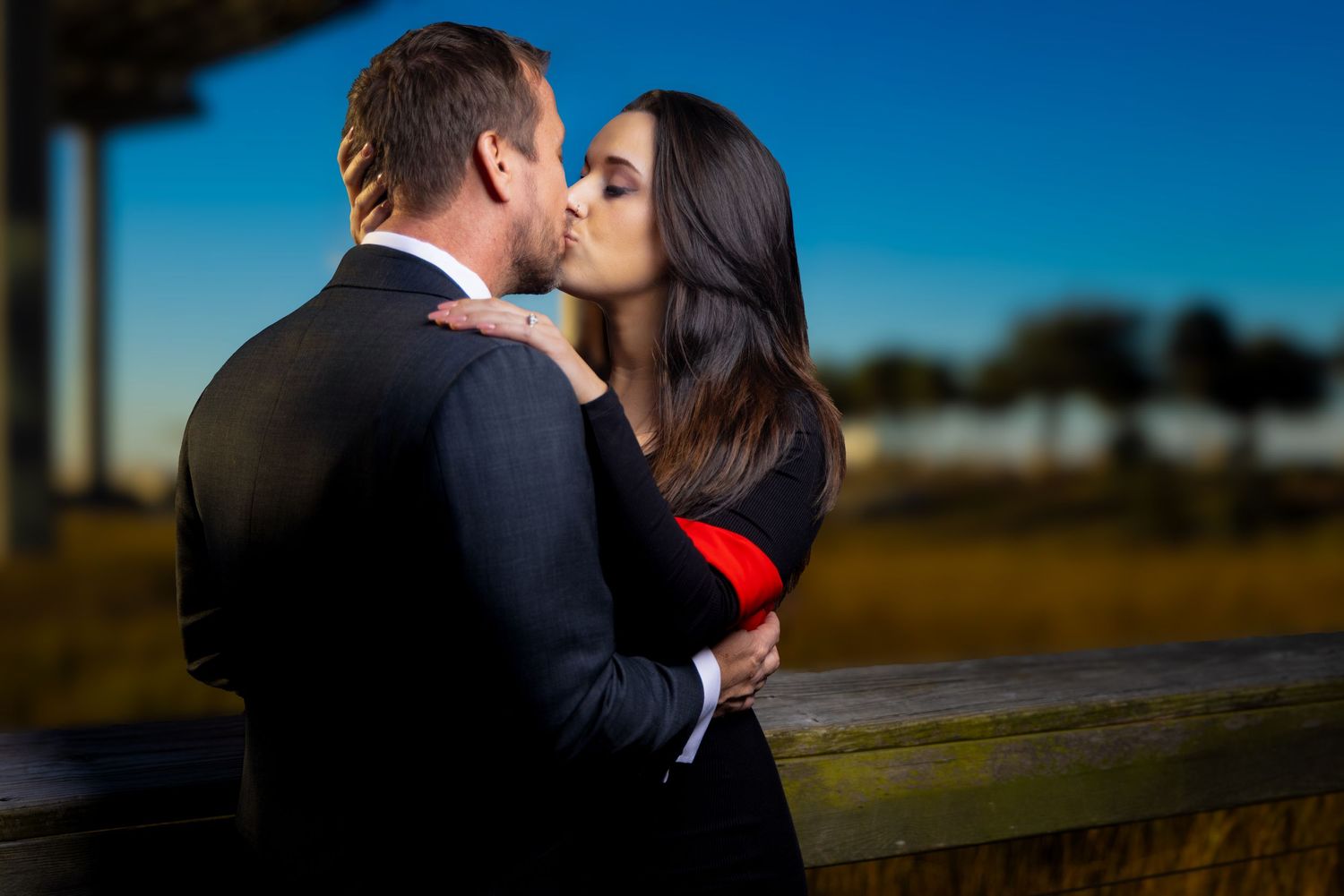 A couple shares a romantic kiss during their outdoor wedding photoshoot at sunset.