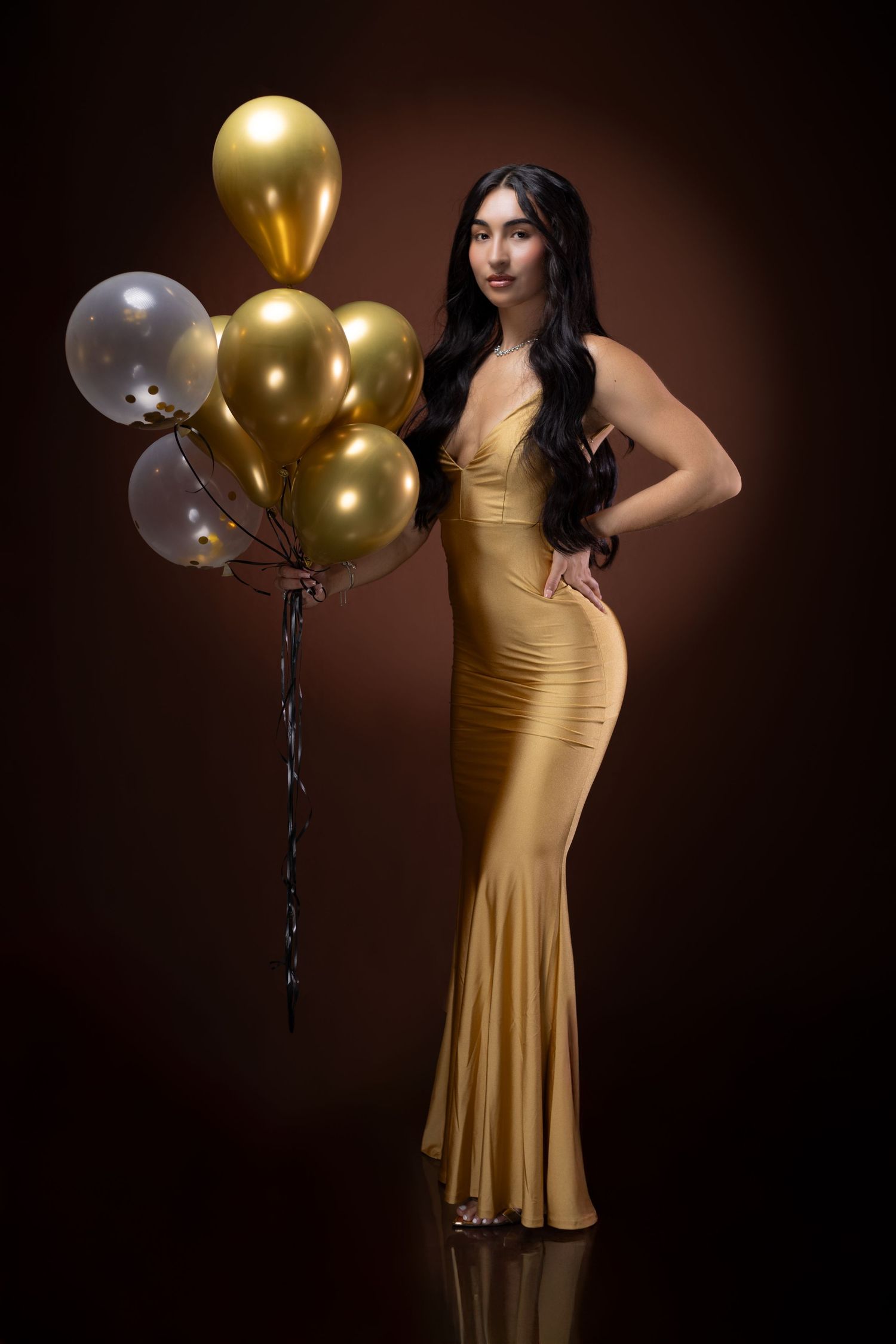 Elegant portrait in gold gown with metallic and clear balloons against dark background. Portrava Creative Studios
