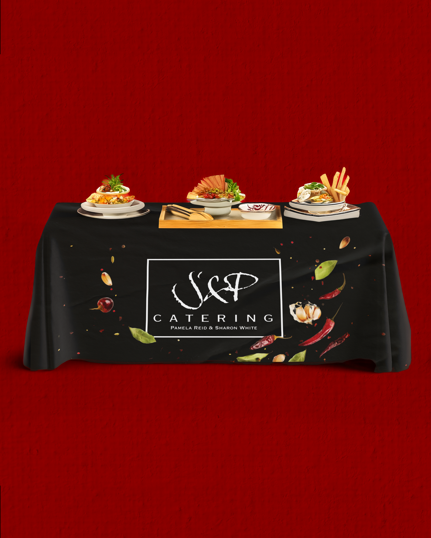 Catering display table with three plated meals and J&P Catering logo banner on black tablecloth. Portrava Creative Studios