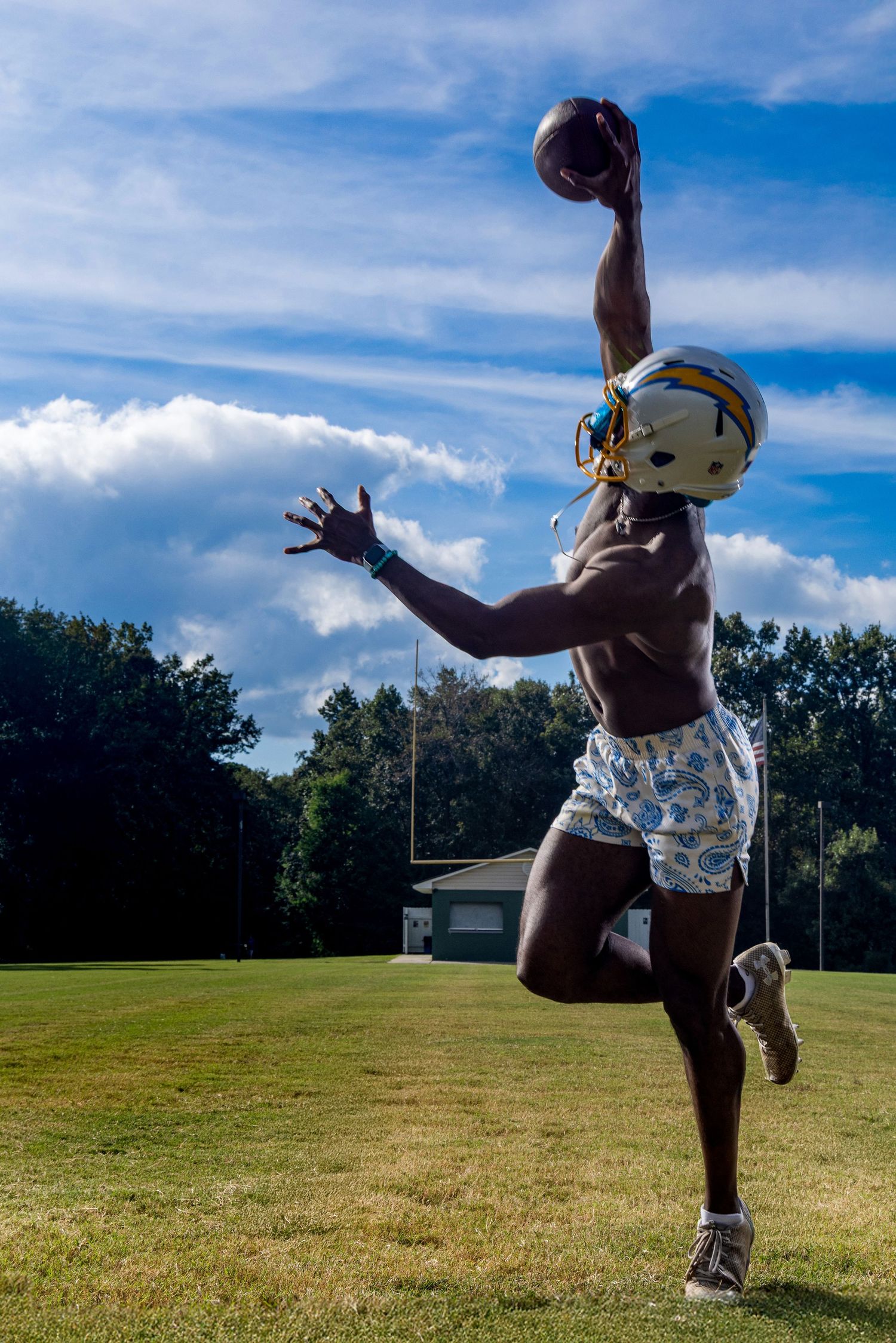 A person jumps and poses playfully on a grassy field under a bright blue sky with white clouds.