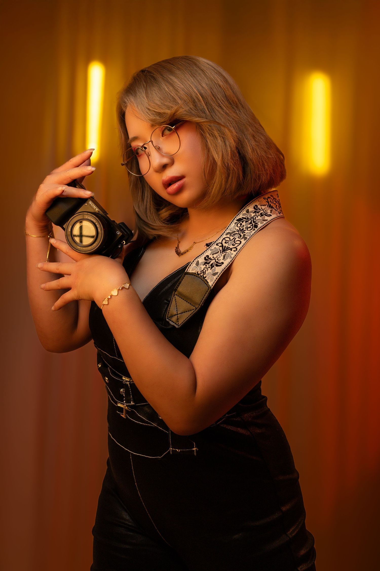 Photographer in black outfit poses with vintage camera in warm lighting. Portrava Creative Studios