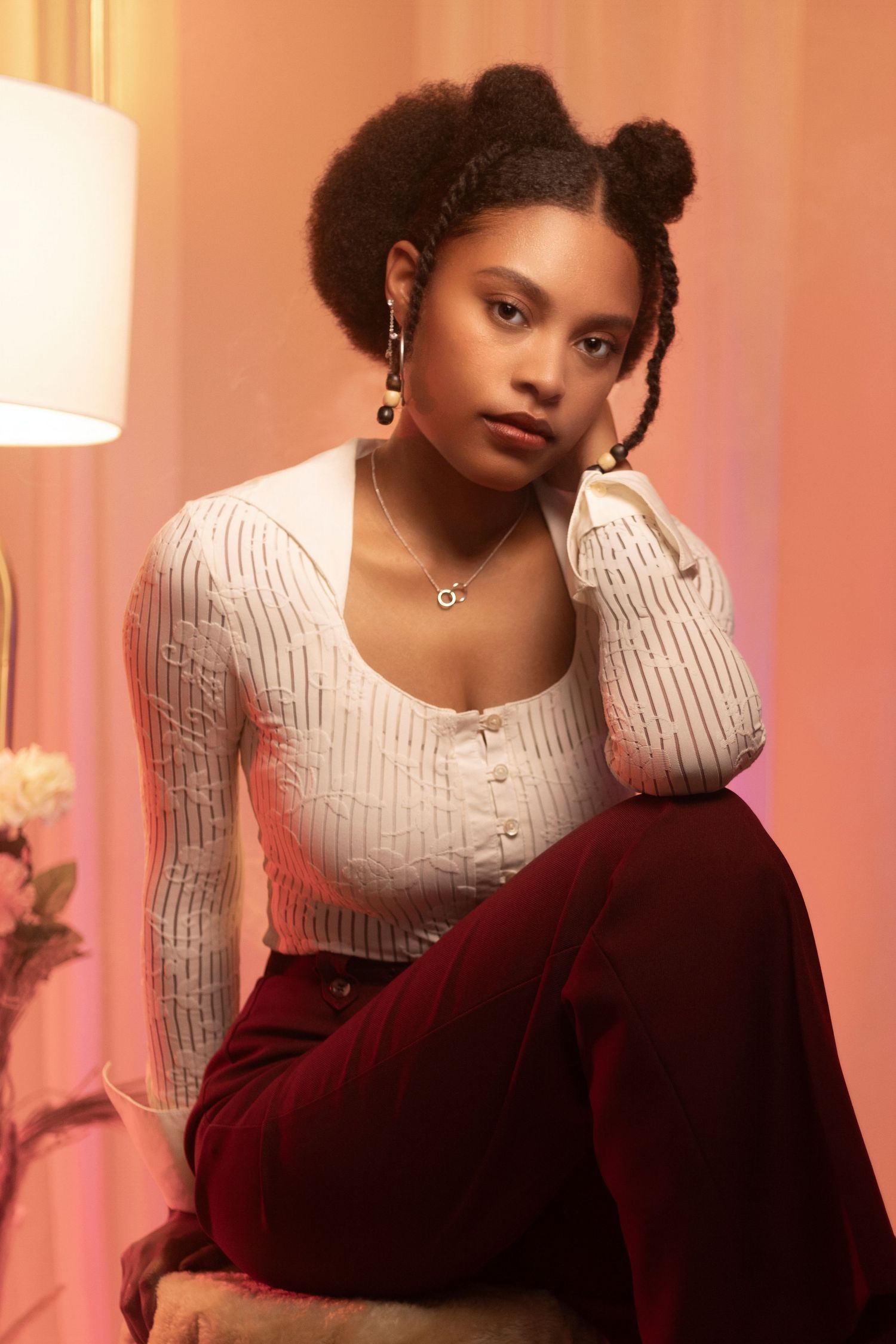 Studio portrait featuring white knit top and burgundy pants against peachy pink backdrop. Portrava Creative Studios