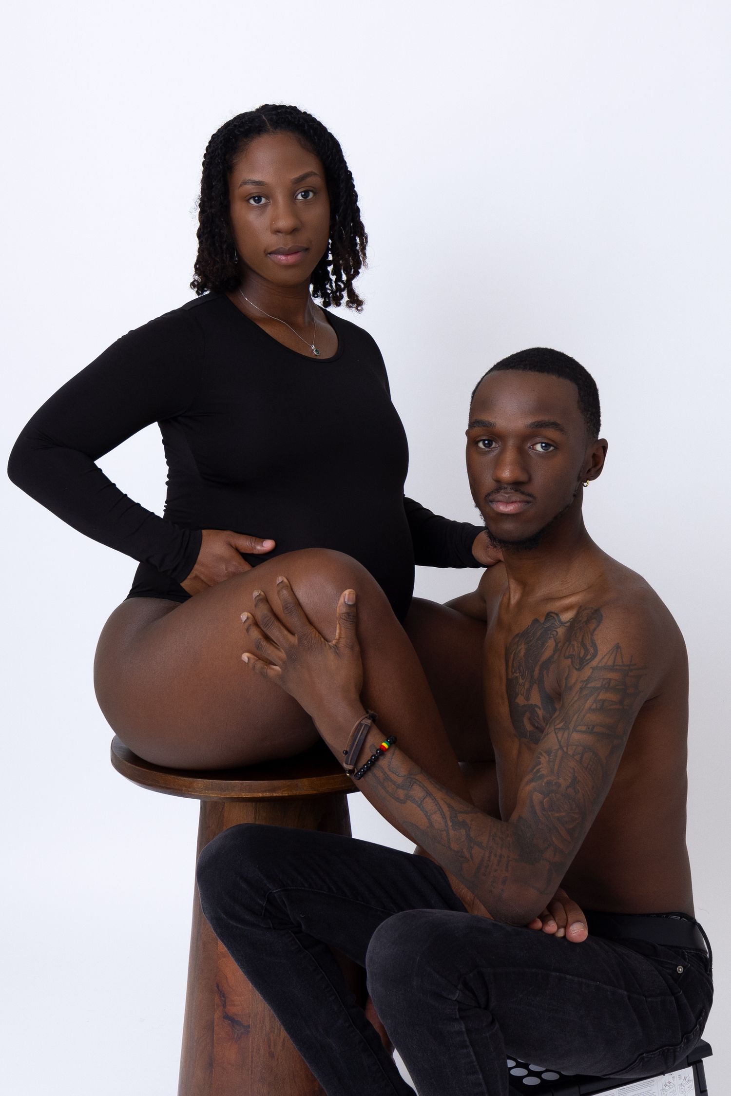 A maternity portrait showing a couple in black clothing against a white background. Portrava Creative Studios