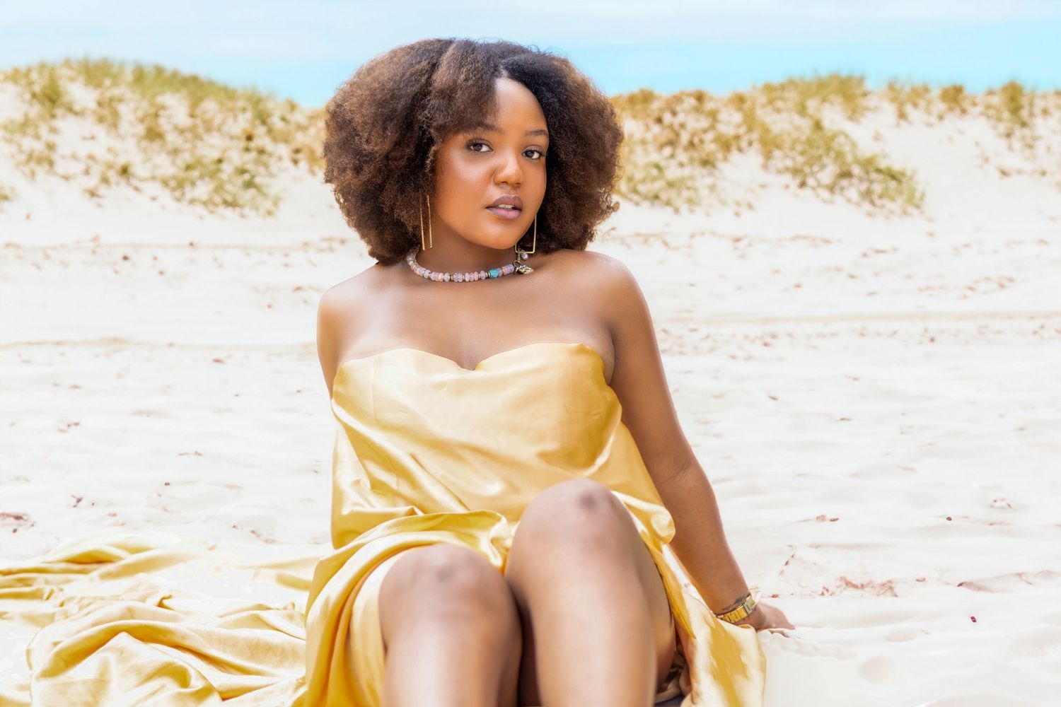 Model in yellow dress poses gracefully on sandy beach. Portrava Creative Studios