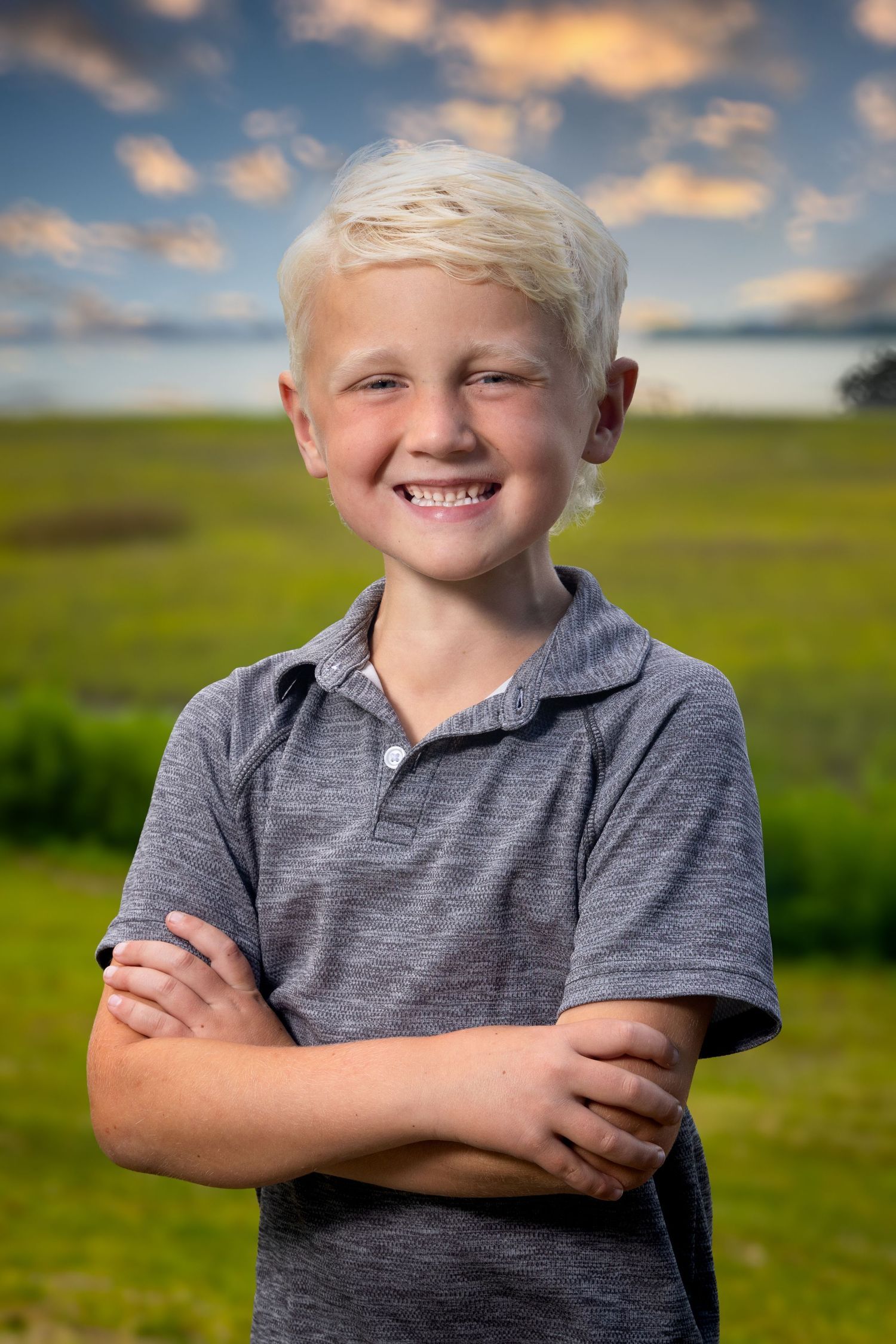 A portrait of someone in a gray polo shirt standing outdoors against green fields and sunset sky. Portrava Creative Studios