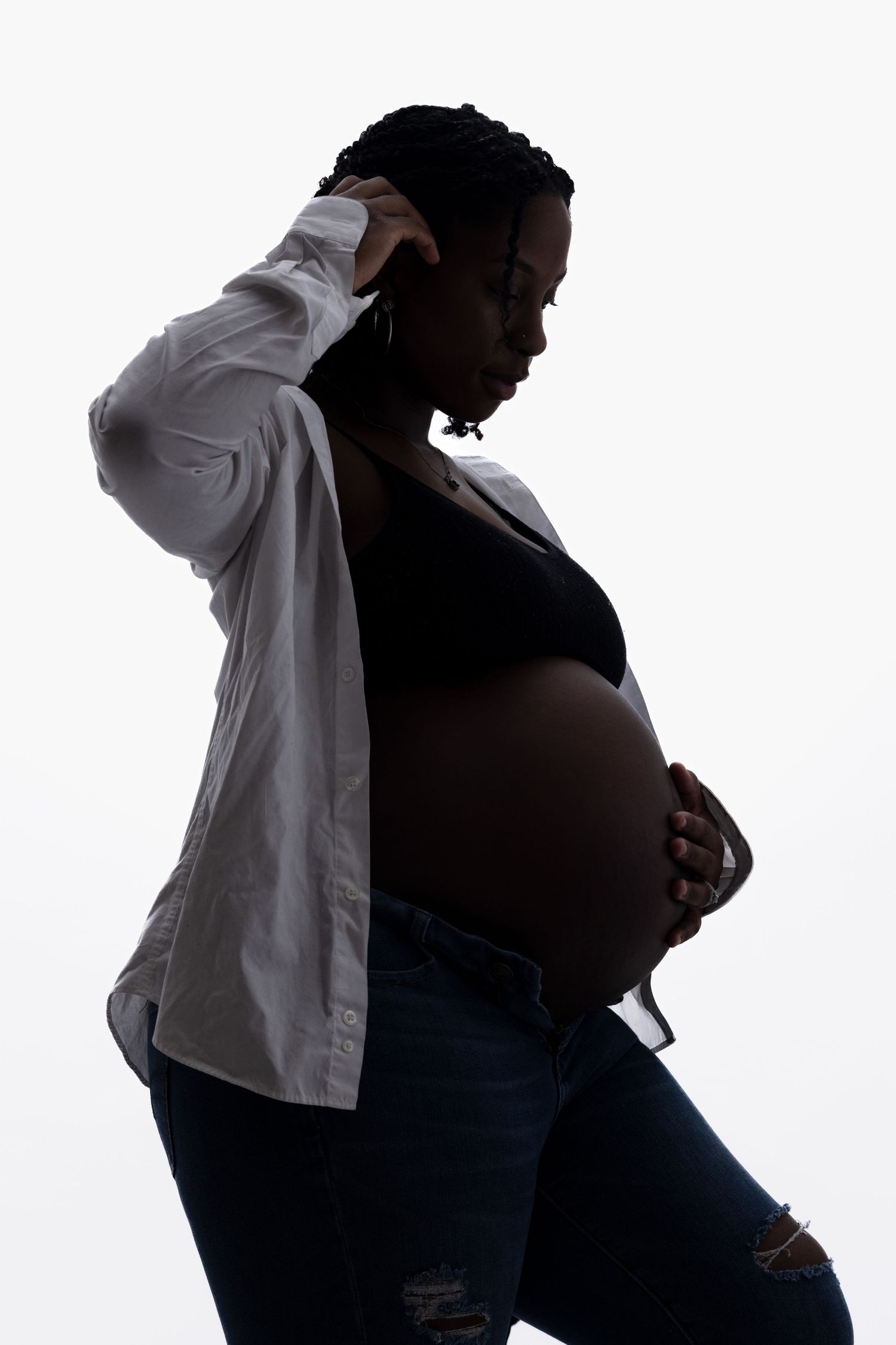 A silhouette of a pregnant figure in profile wearing a white shirt against a light background. Portrava Creative Studios
