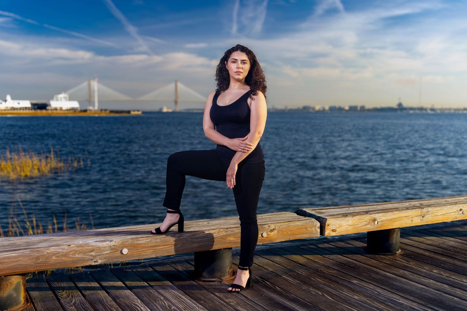 Waterfront fashion portrait with bridge visible in background during golden hour. Portrava Creative Studios