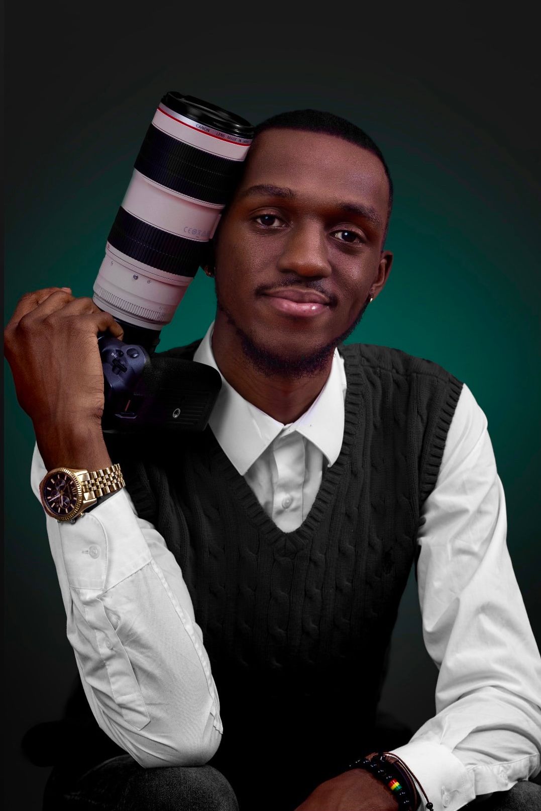 Professional photographer in white shirt and black vest holds camera lens against dark studio backdrop.