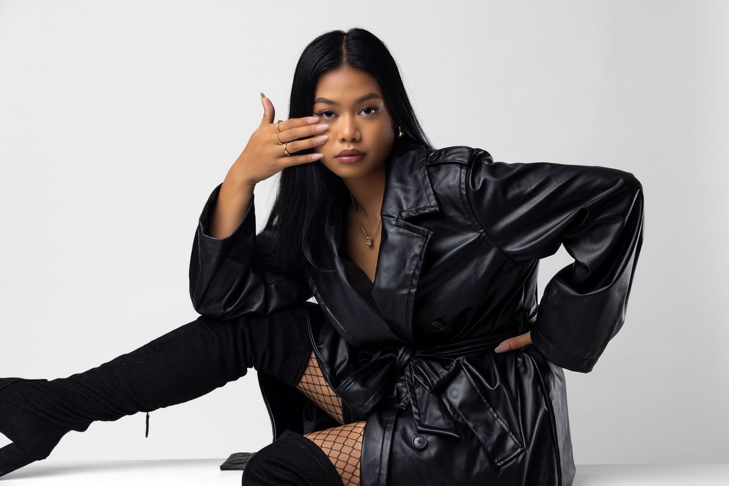 Stylish pose in oversized black leather jacket against minimalist white studio setting. Portrava Creative Studios