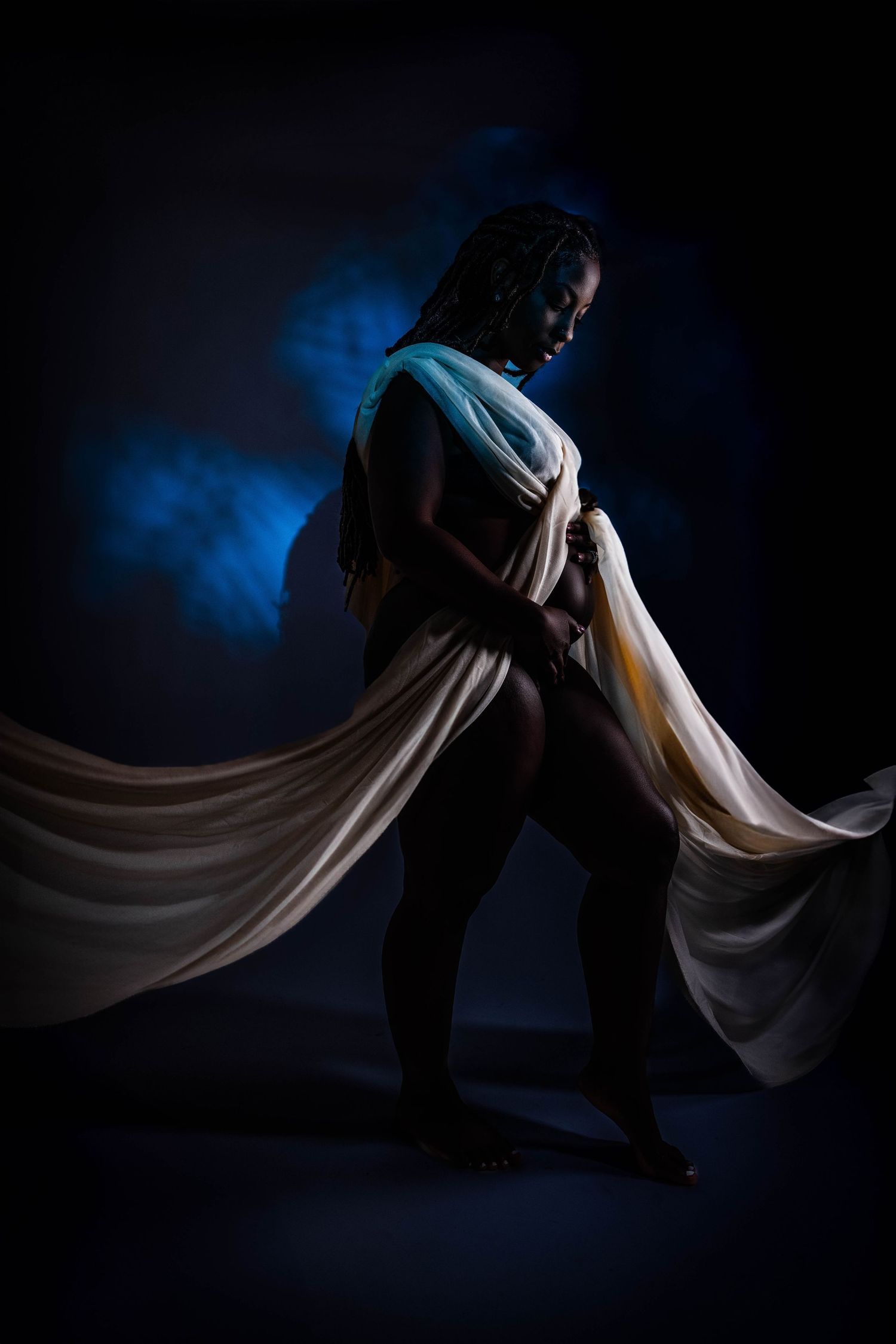 Dramatic low-key portrait with flowing white fabric against dark blue smoky background. Portrava Creative Studios