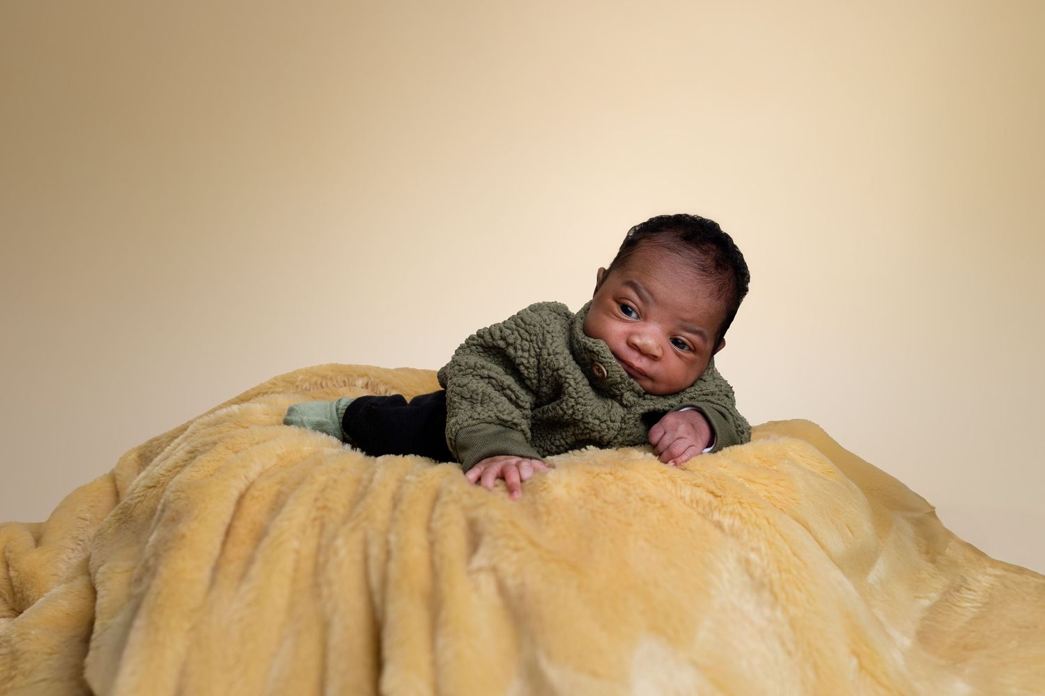 Baby in a green sweater resting peacefully on a soft yellow blanket against beige background. Portrava Creative Studios