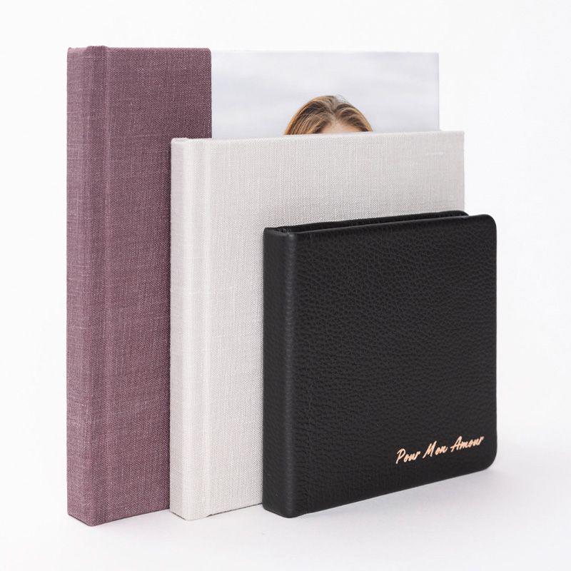 Collection of photo albums in different materials including black leather, linen, and purple fabric.