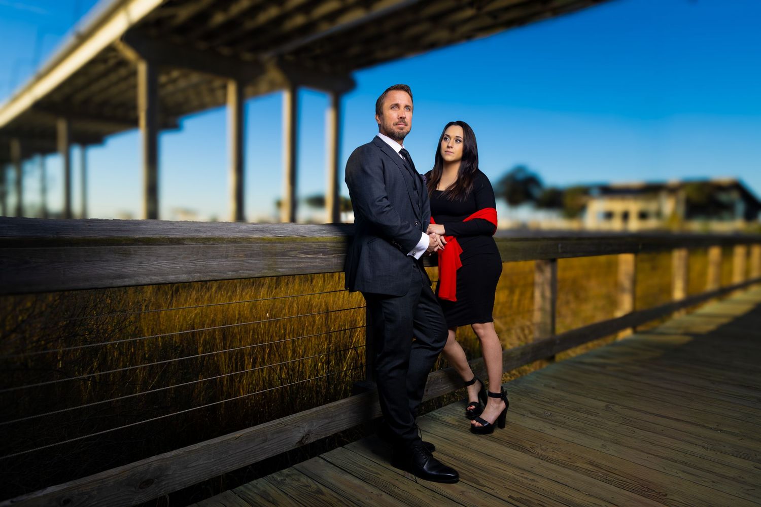 Two people sit together on a wooden boardwalk overlooking coastal marshland during golden hour.