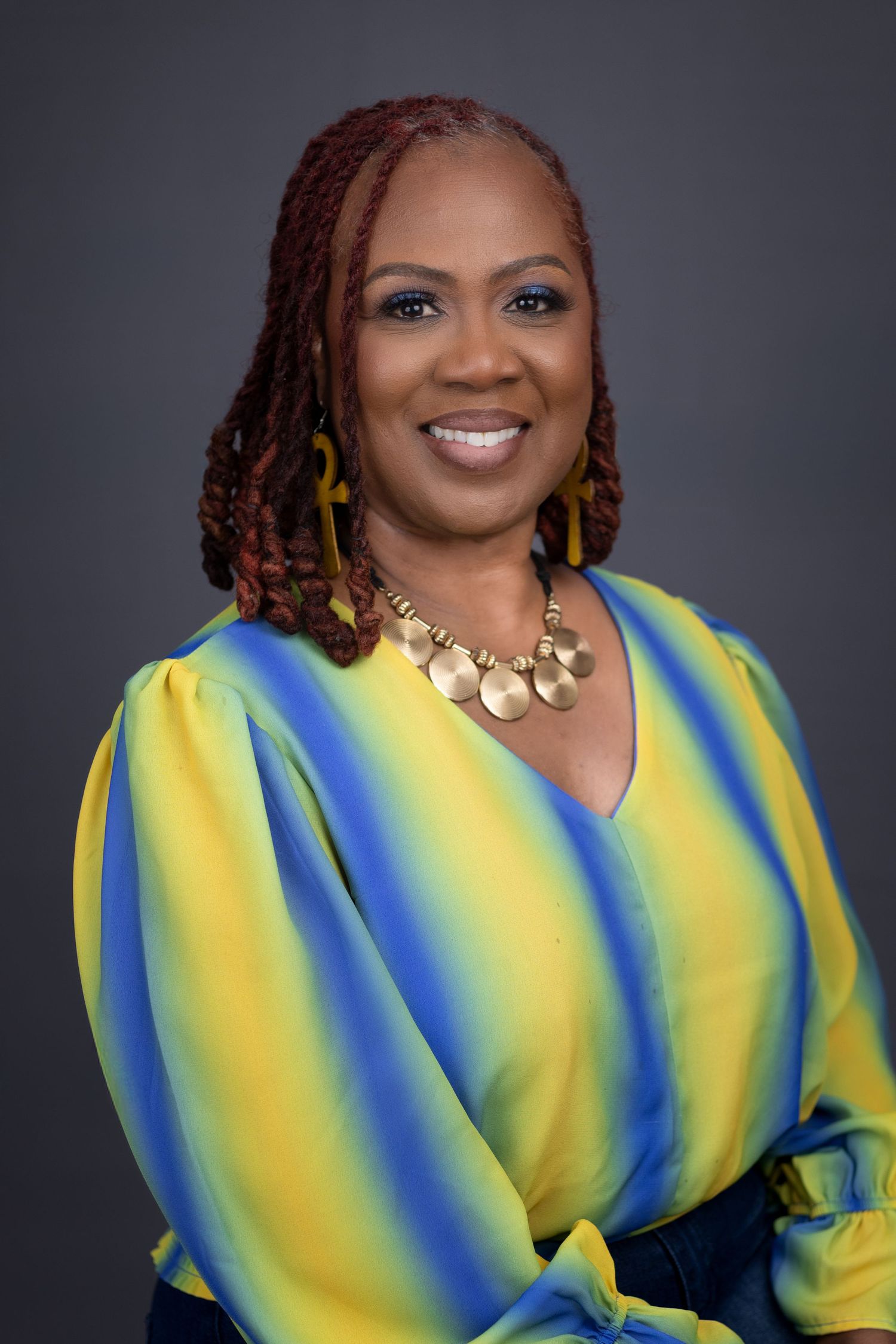 Professional portrait of a woman in vibrant yellow and blue striped top with statement necklace. Portrava Creative Studios