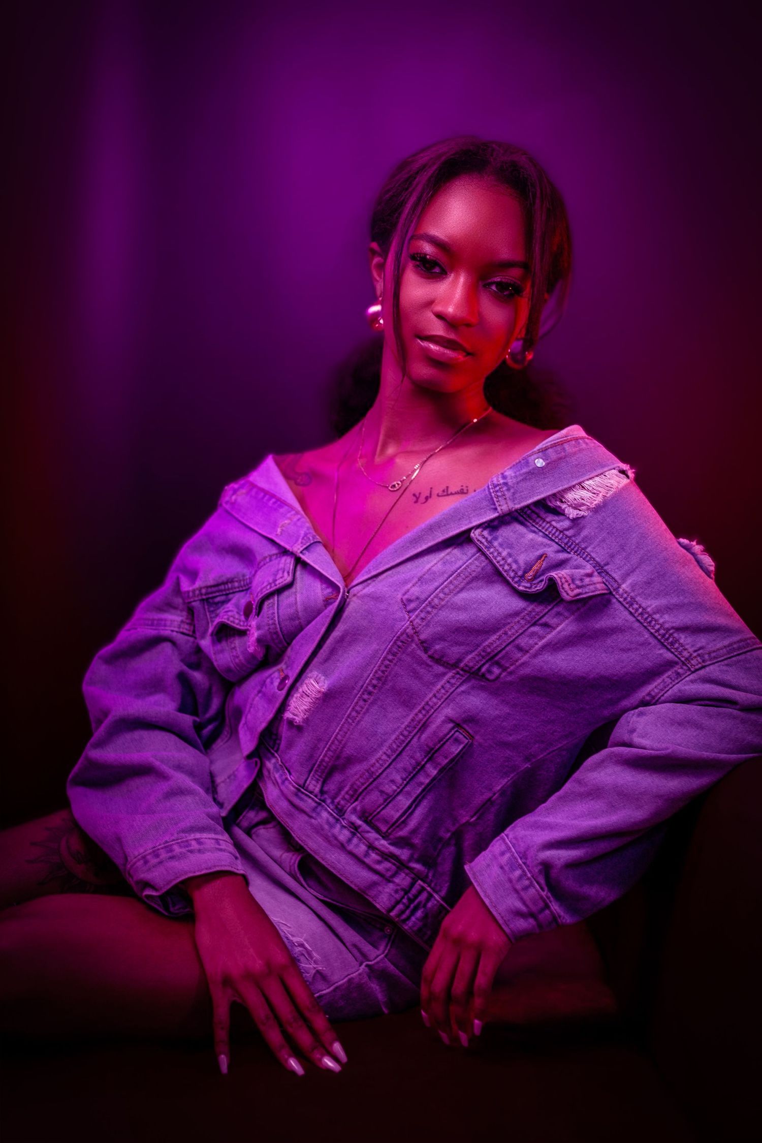 Fashion portrait with purple lighting and denim jacket against dark background. Portrava Creative Studios