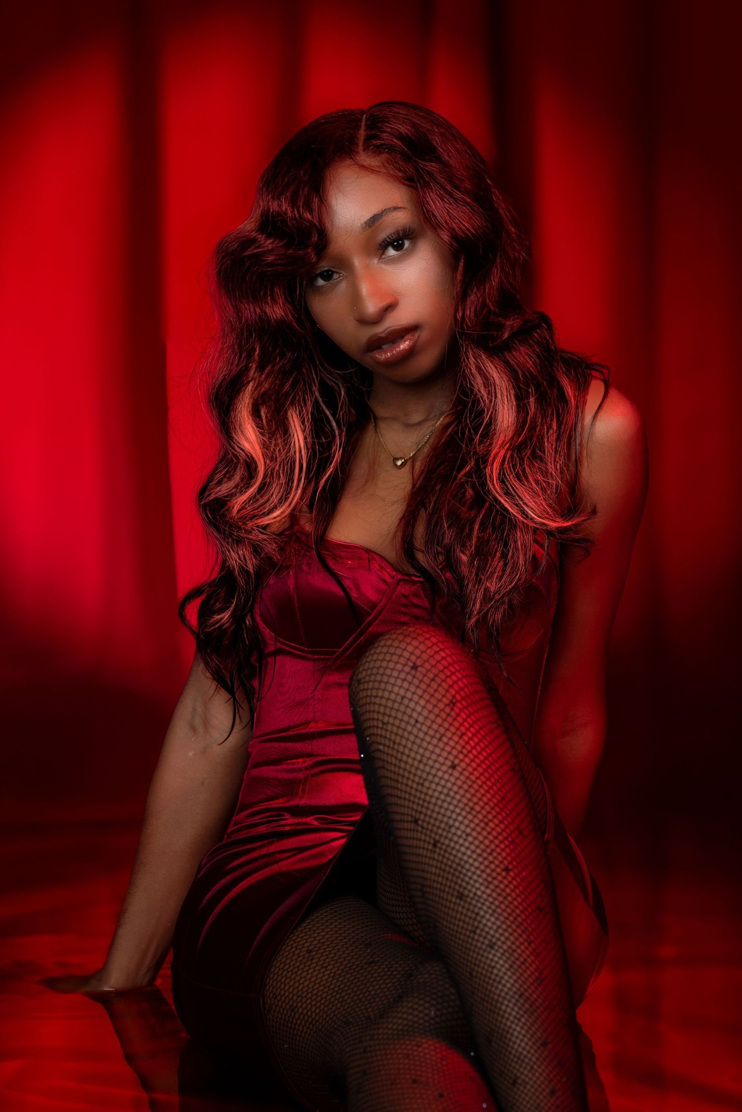Sultry fashion portrait in red dress and fishnets against dramatic red background. Portrava Creative Studios