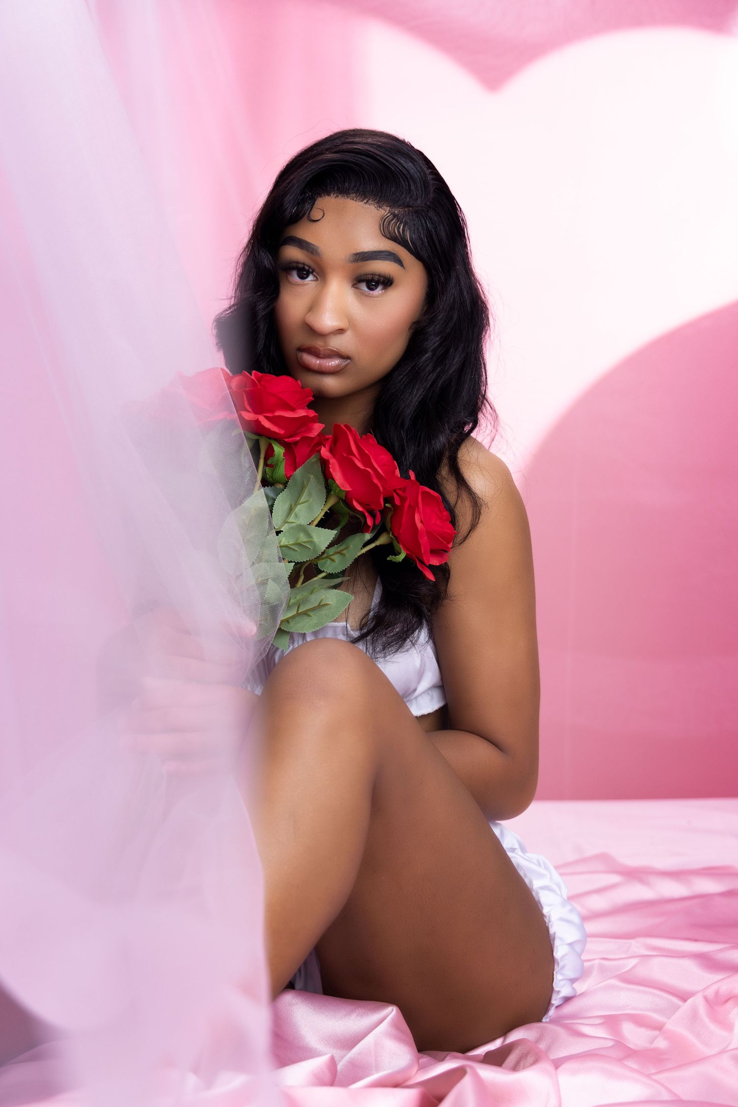 Romantic portrait session with red roses against pink heart-shaped backdrop. Portrava Creative Studios