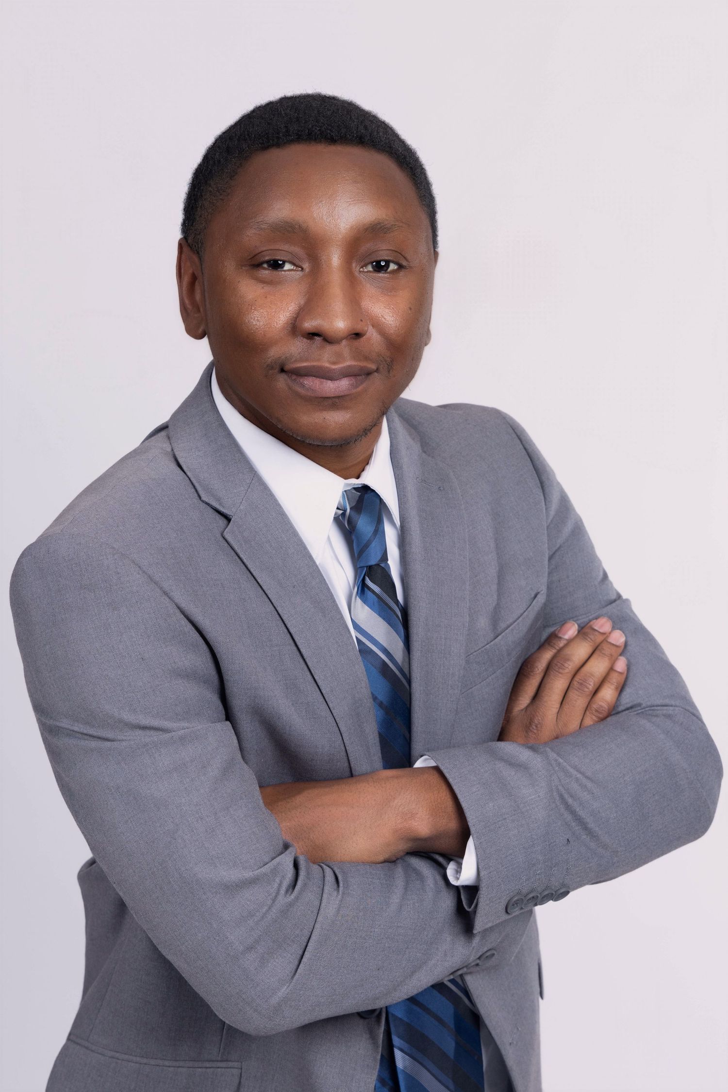 Professional portrait of someone in a grey suit and striped tie with arms crossed against light background. Portrava Creative Studios.