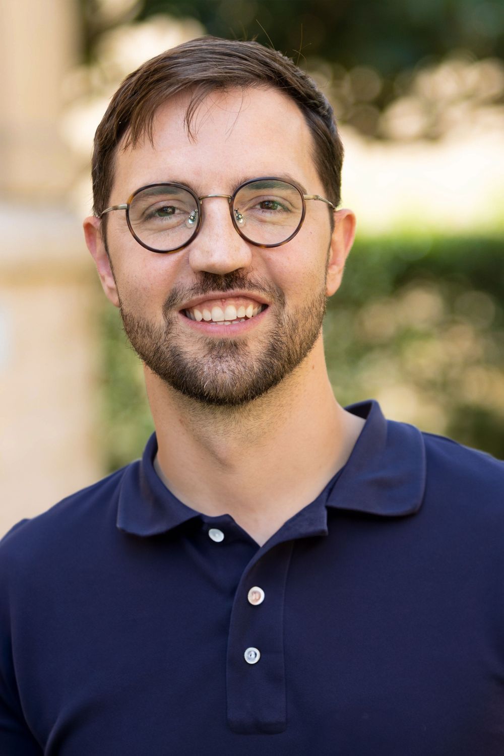 Professional portrait of person wearing glasses and navy polo shirt against blurred background. Portrava Creative Studios