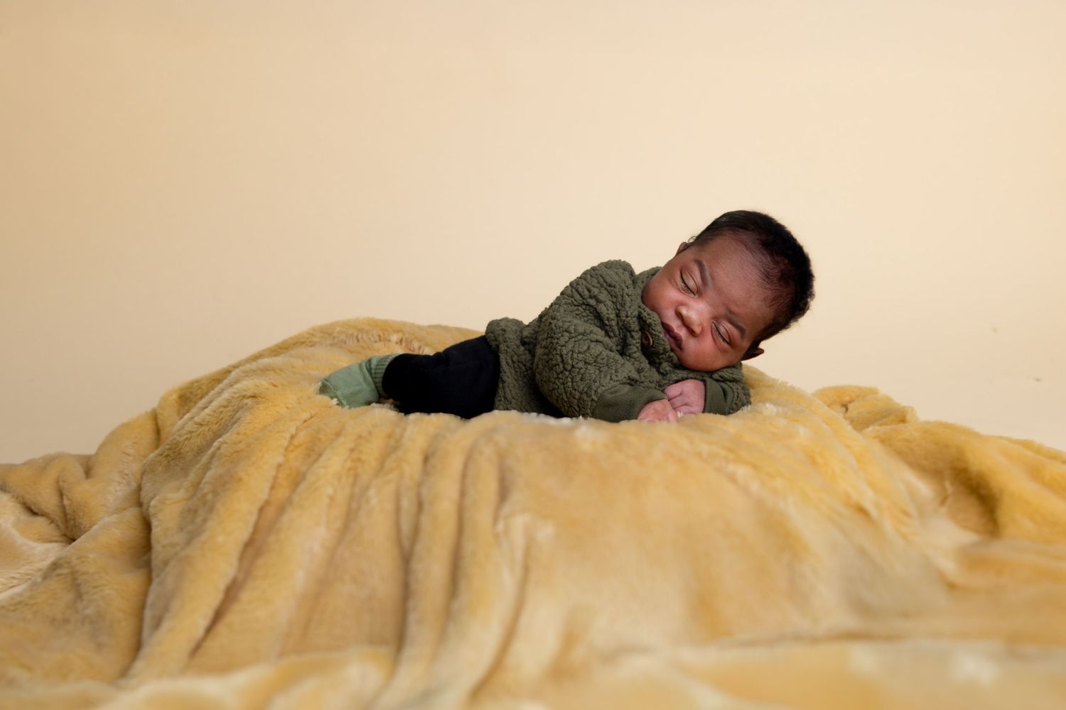 A sleeping baby in green clothing rests peacefully on a plush yellow blanket. Portrava Creative Studios