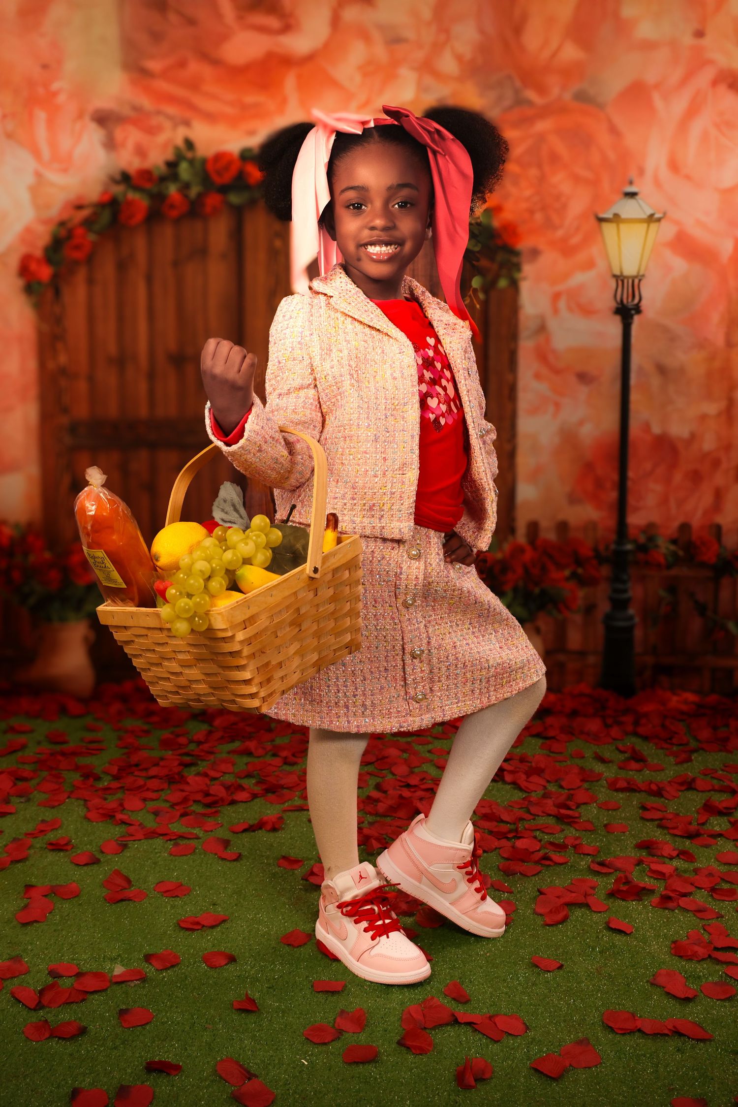 A young figure in a pink sweater and dress holds a basket of fruit while standing on rose petals against a warm-toned backdrop. Portrava