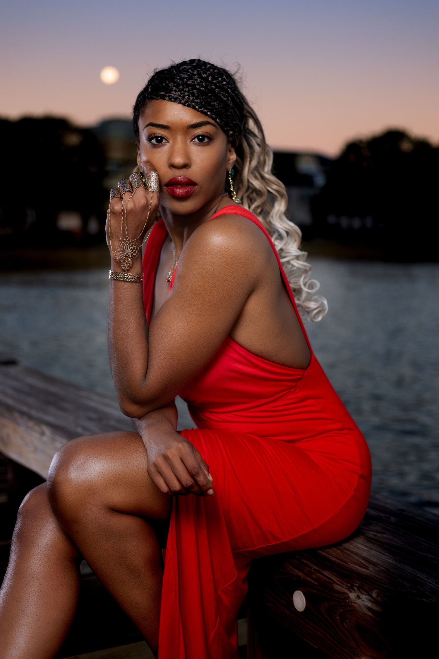 Glamorous portrait at dusk featuring red dress and statement jewelry by the water. Portrava Creative Studios
