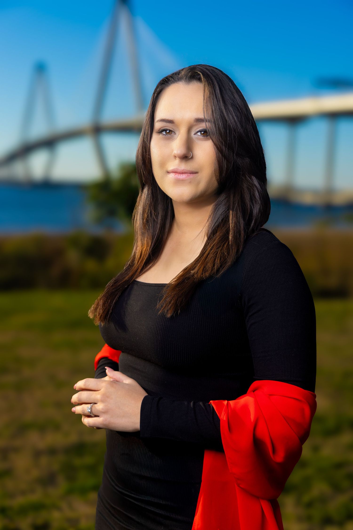 A series of outdoor portrait photos showing someone in a black top and red shawl against a blue sky and bridge background.