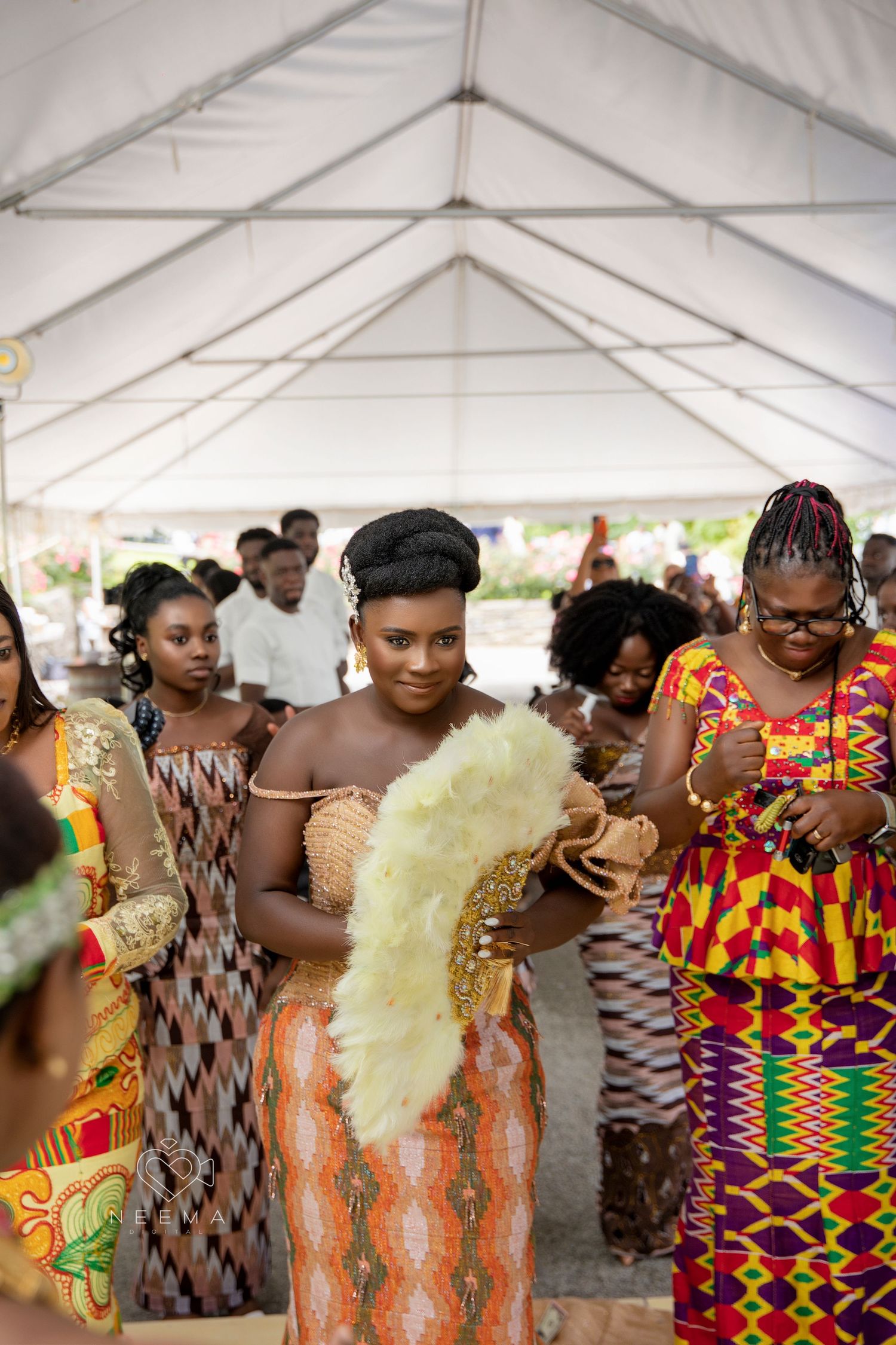 Celebration under white tent with attendees wearing traditional African prints.