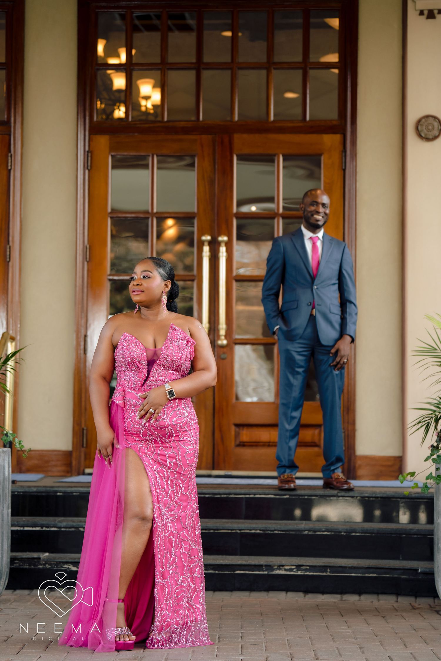 Glamorous couple poses on steps, wearing pink gown and navy suit.
