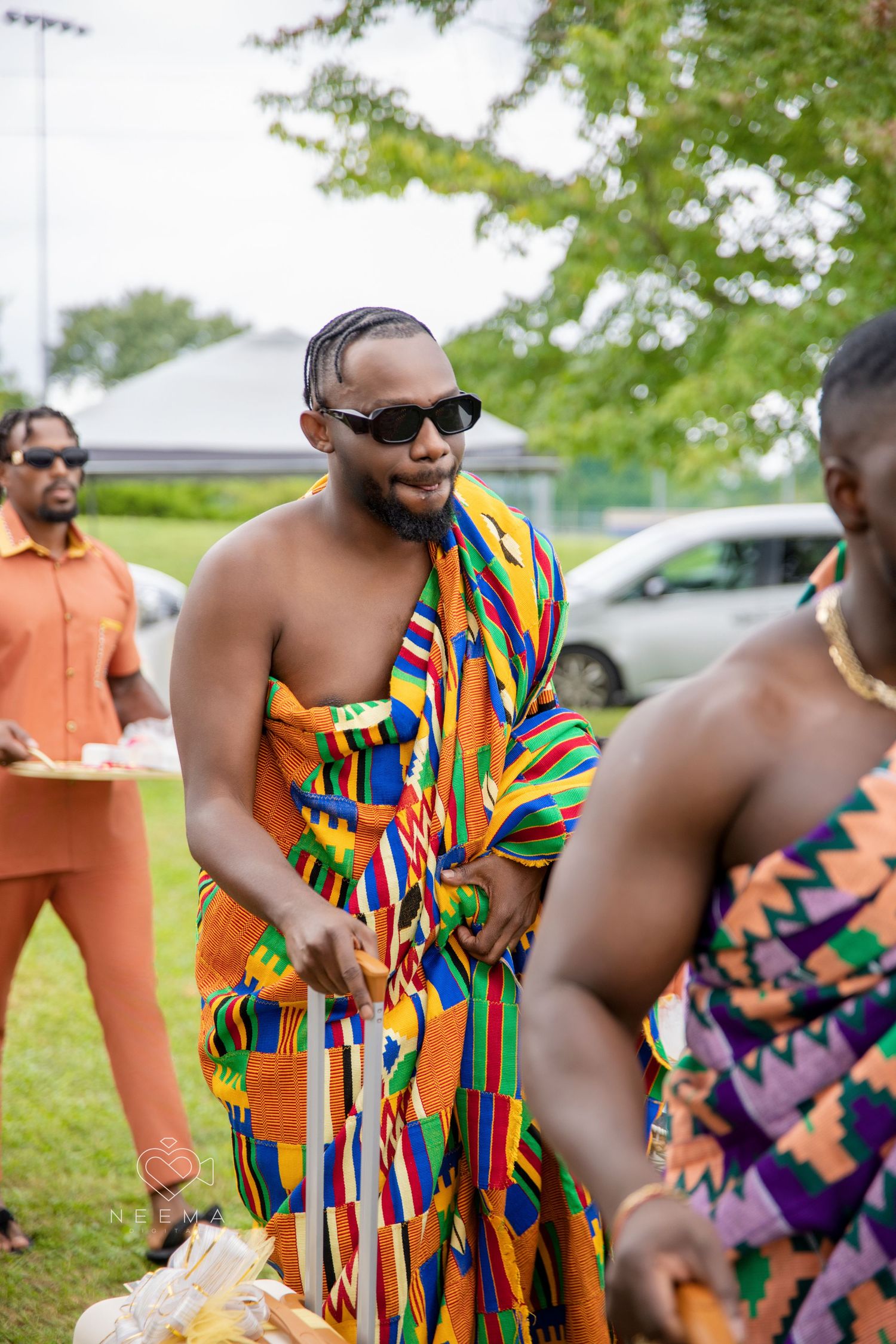 People in colorful kente cloth and traditional African attire gather outdoors.