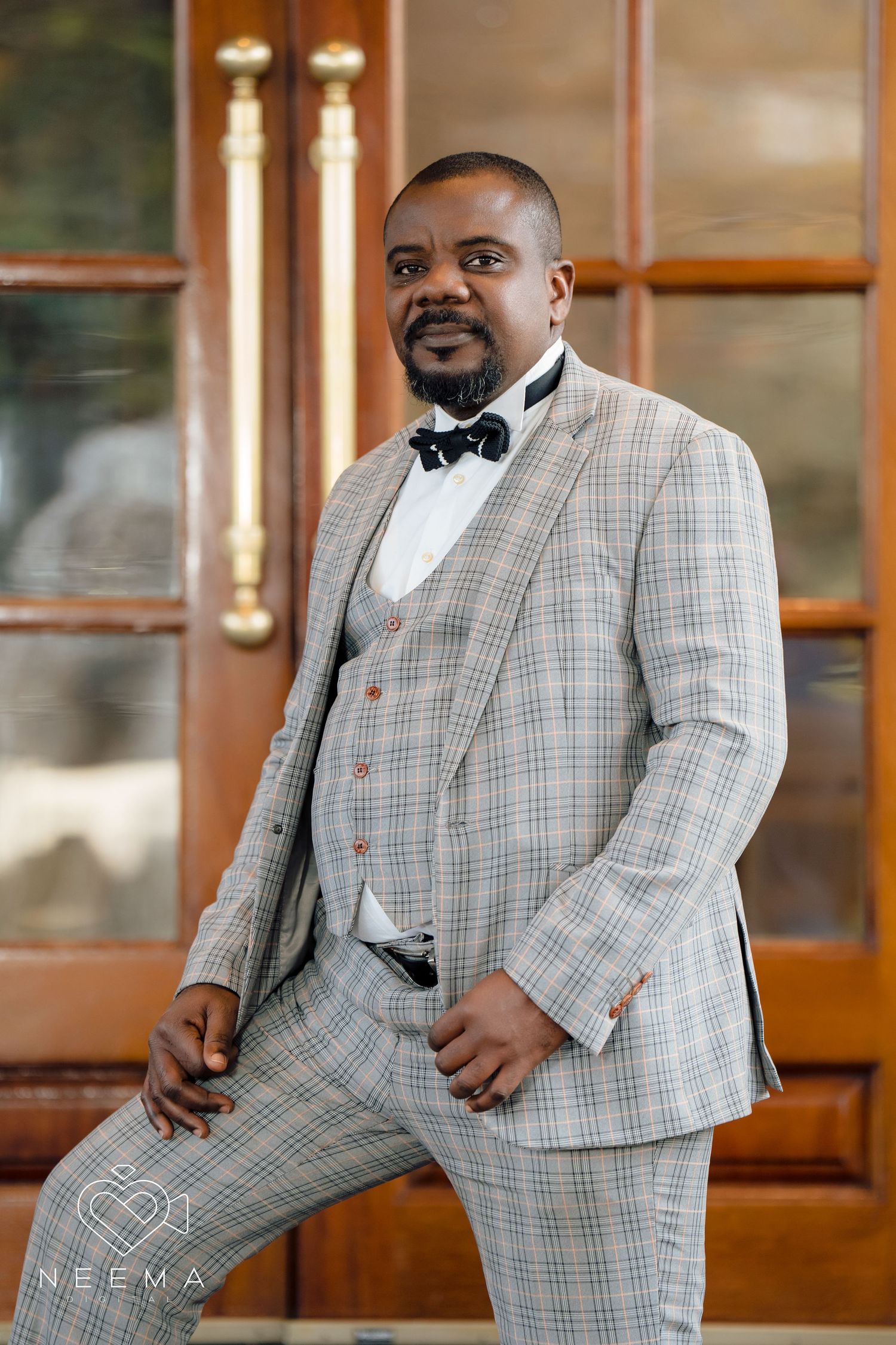 Dapper grey plaid three-piece suit with bow tie photographed in an elegant doorway.