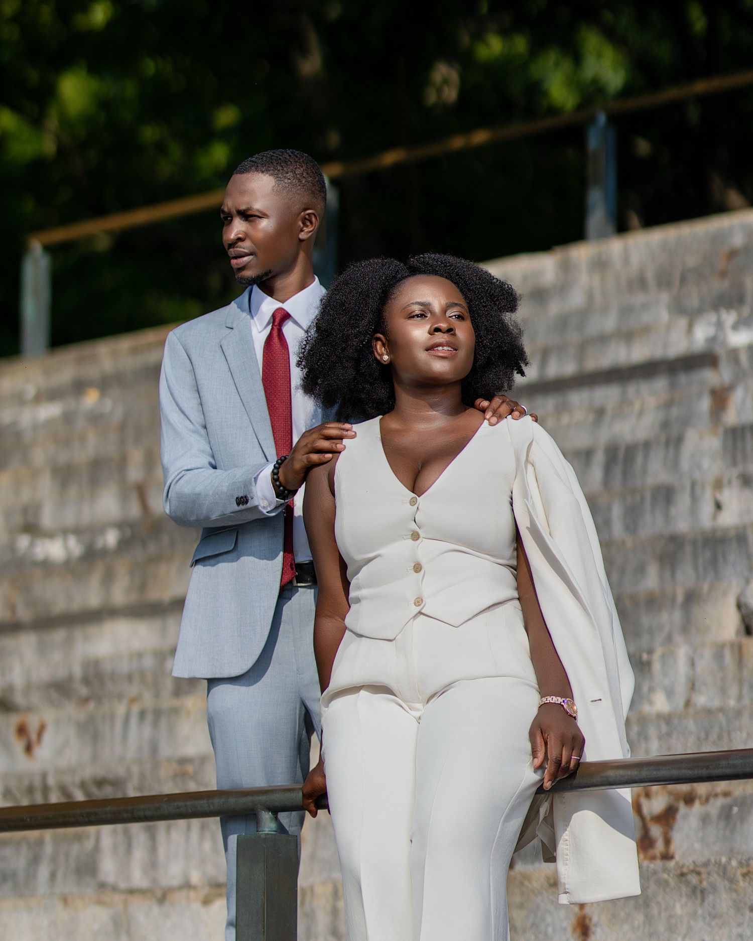 Elegant couple in formal attire pose on concrete steps outdoors.