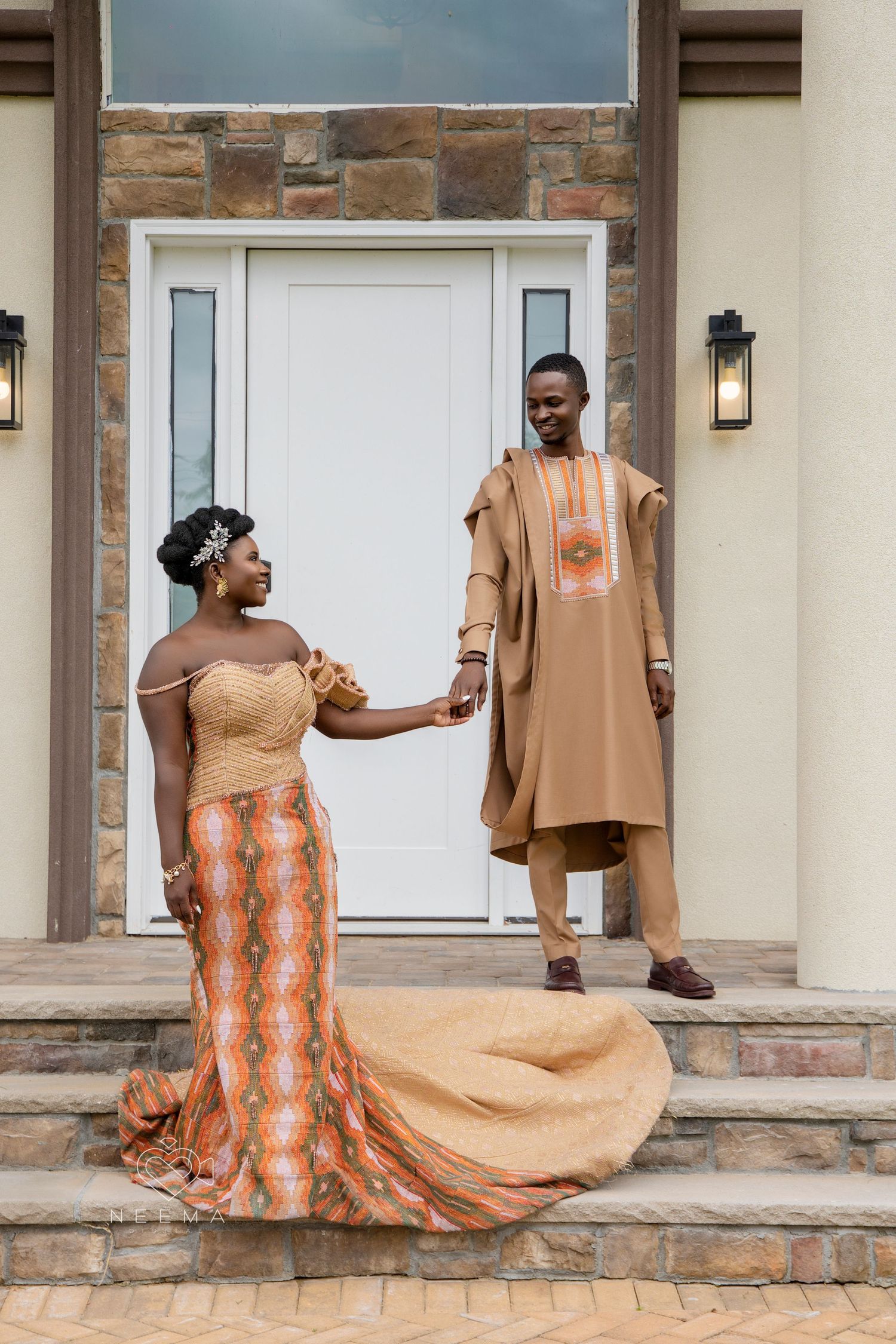 Couple in traditional formal attire posing on stone steps in front of white door.