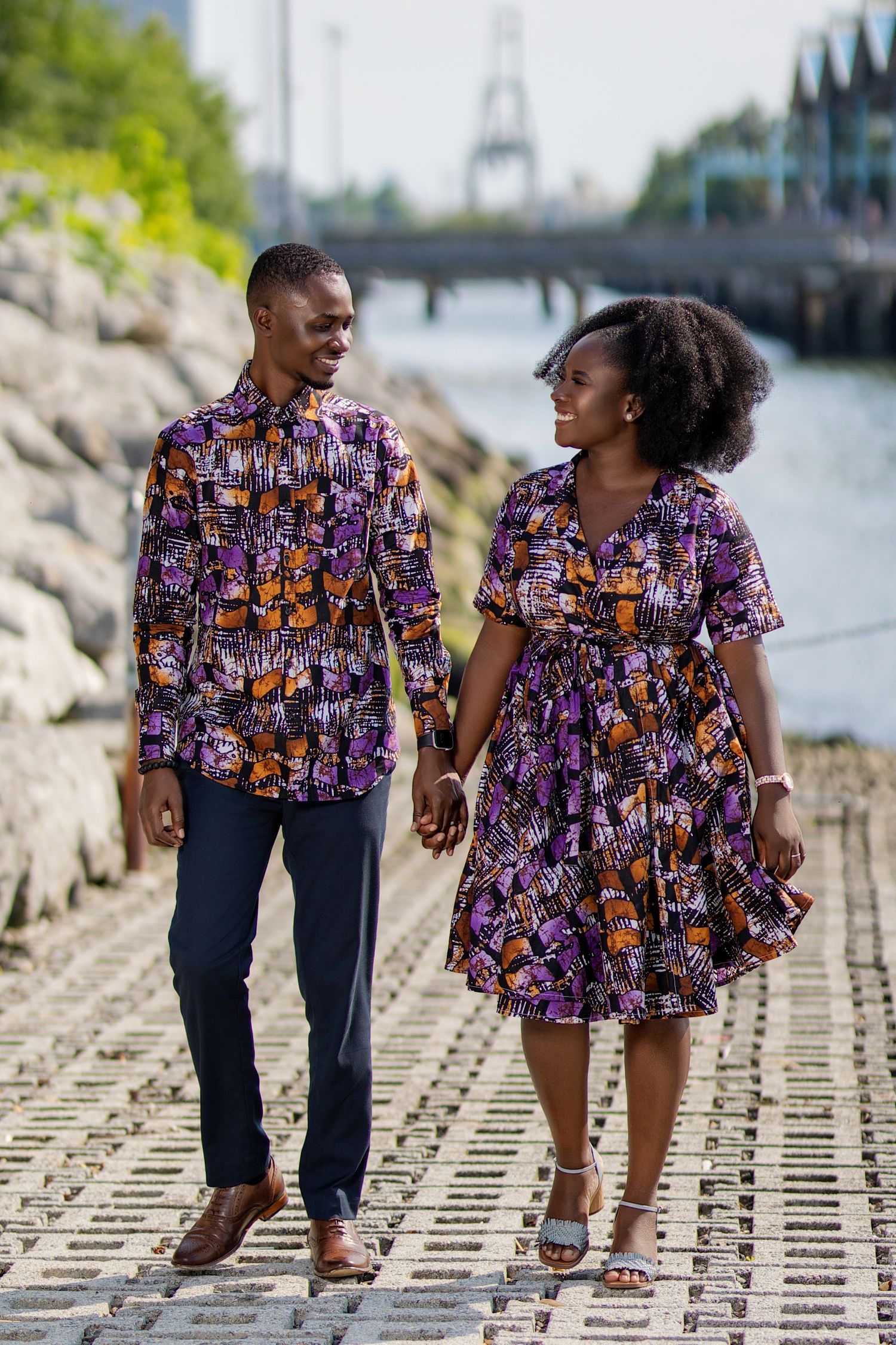 Couple wearing matching floral print outfits walking along waterfront path.