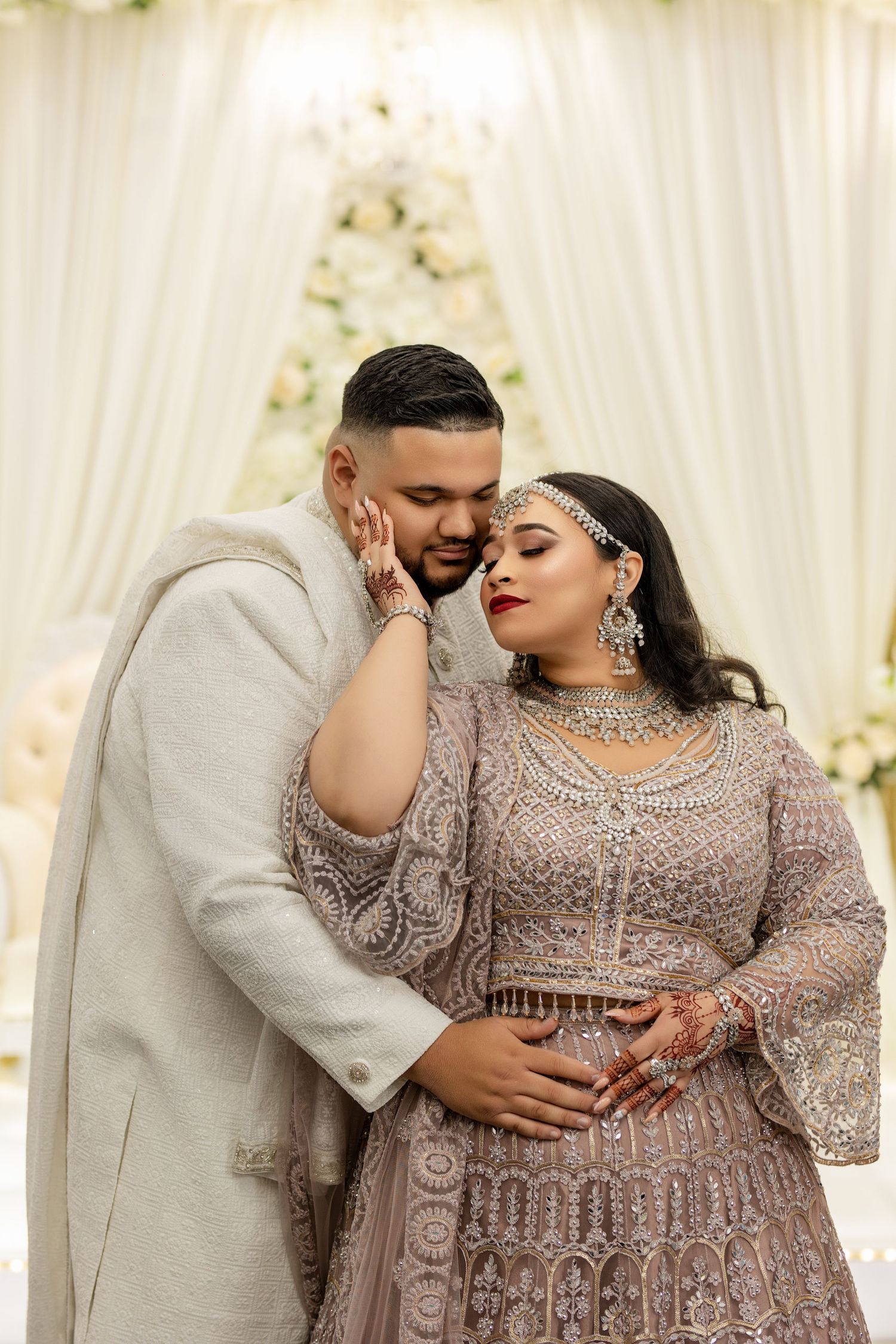 A couple embraces in traditional South Asian wedding attire featuring intricate beadwork and embellishments.