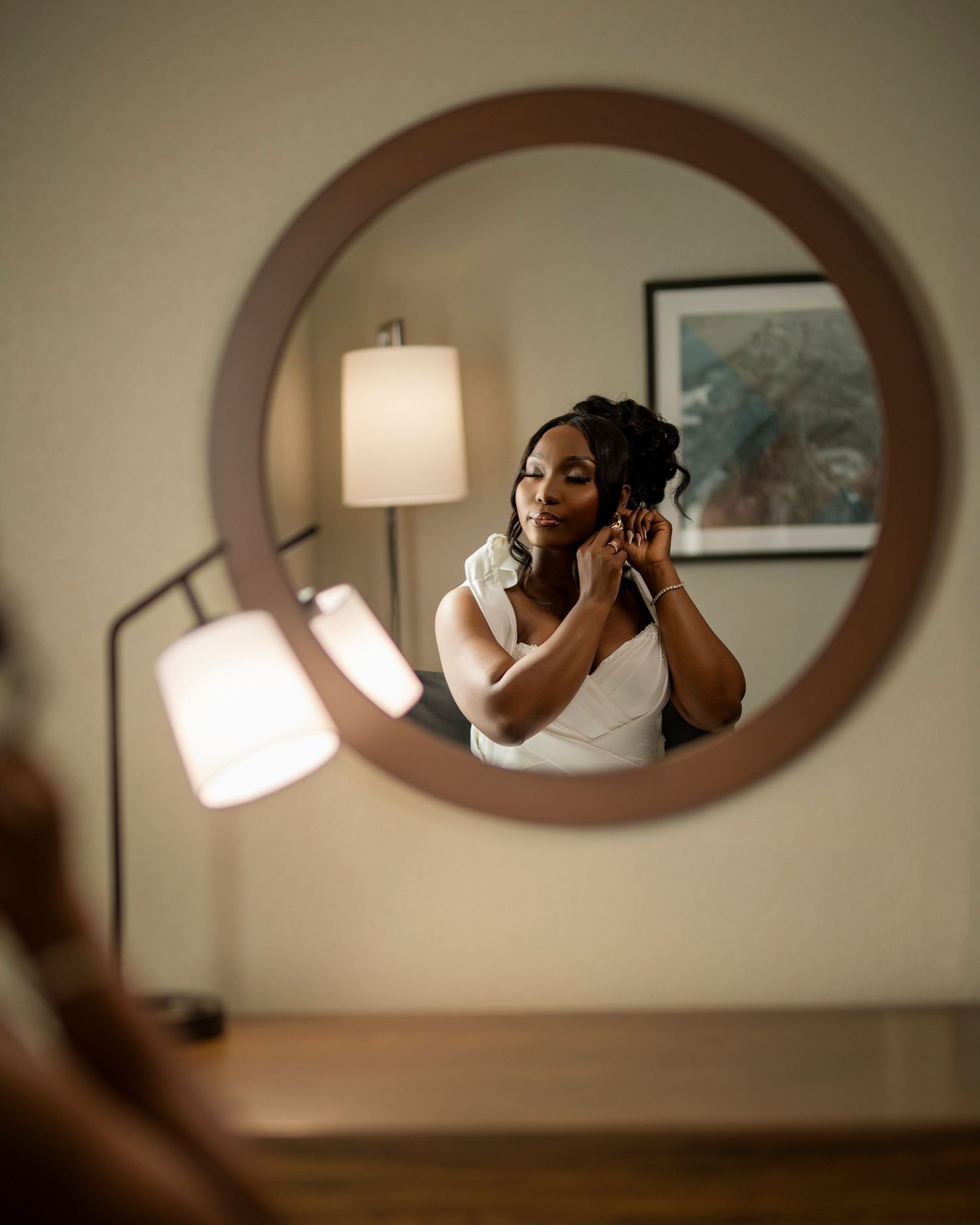 Artistic mirror reflection shot of bride putting on earrings in circular frame.
