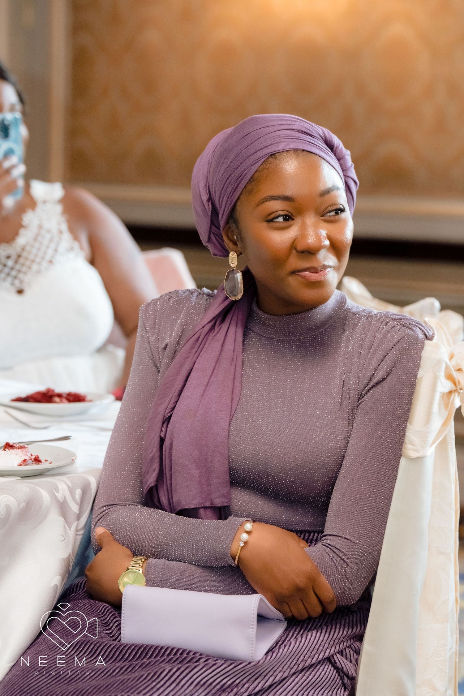 Guest in purple attire with matching headscarf seated at formal event table.