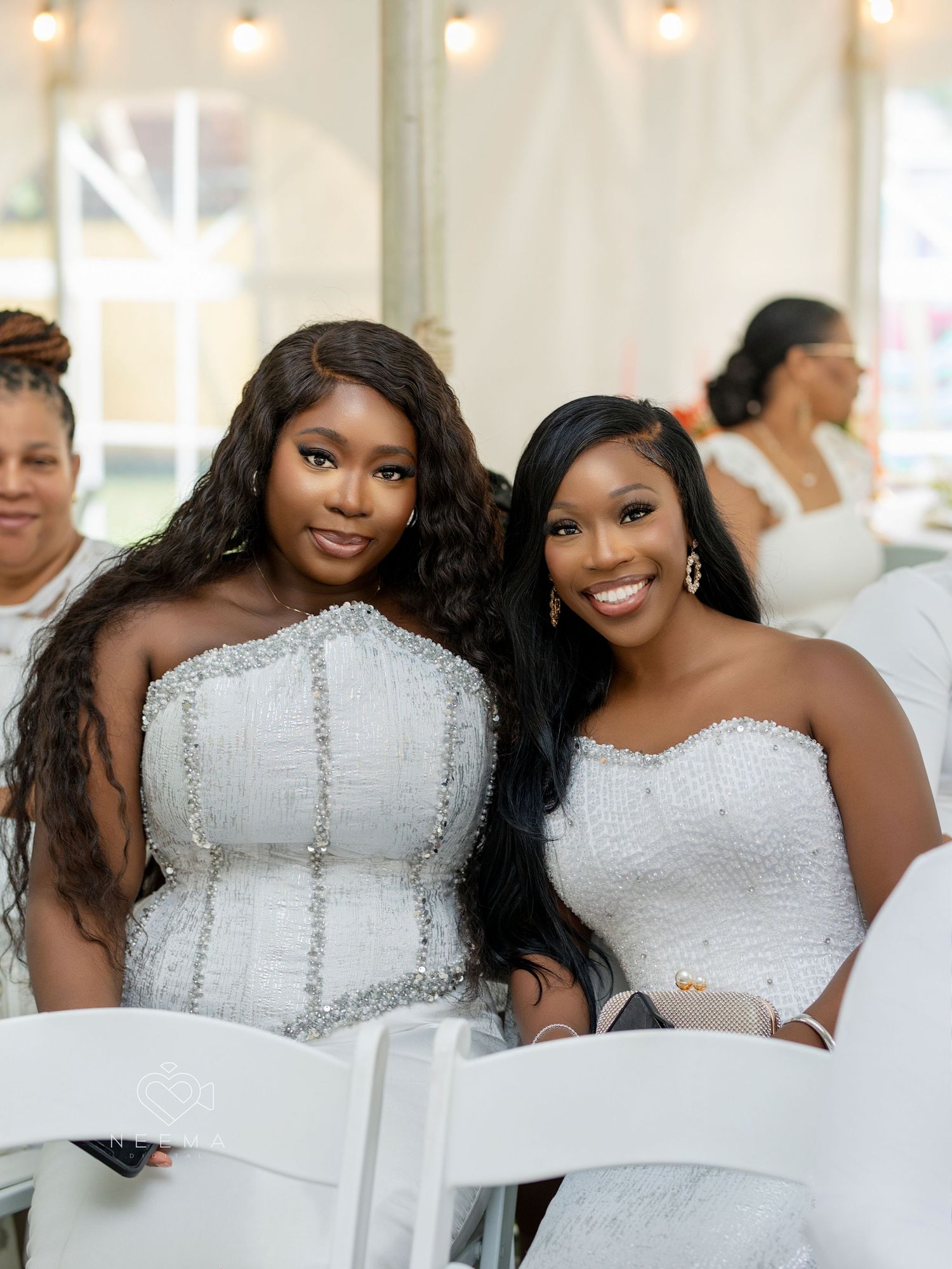 Three people in elegant white formal gowns smile while seated at an event.