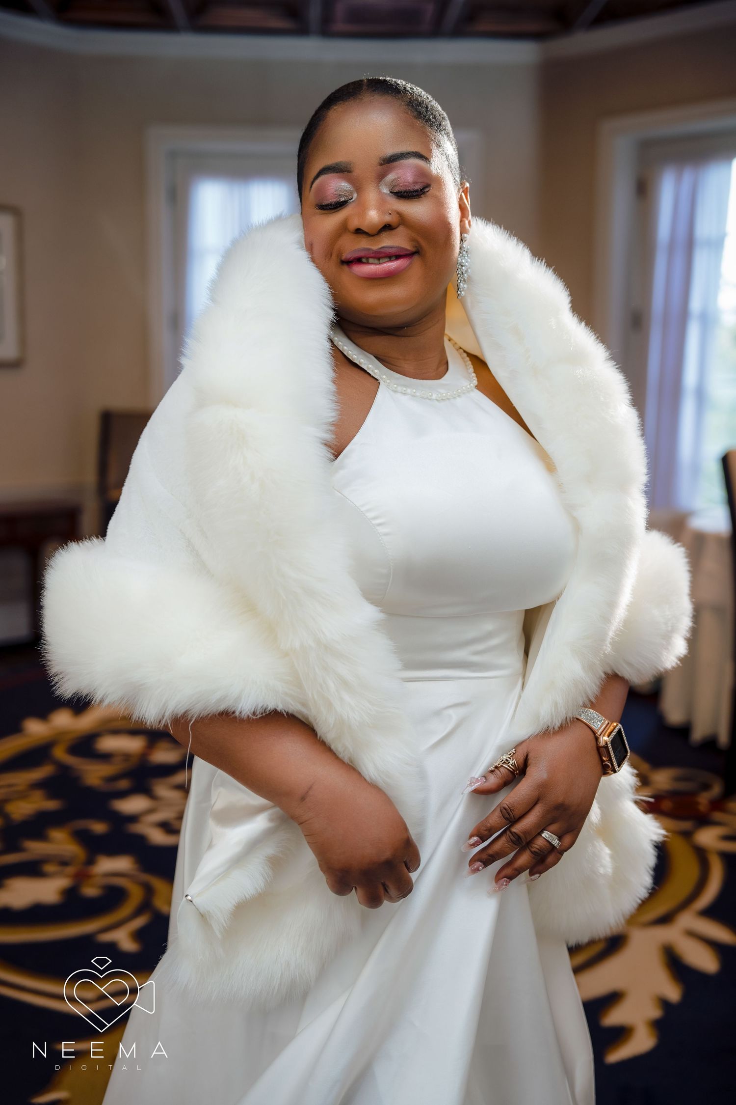 Bride in elegant white dress with plush fur wrap smiles in indoor setting.