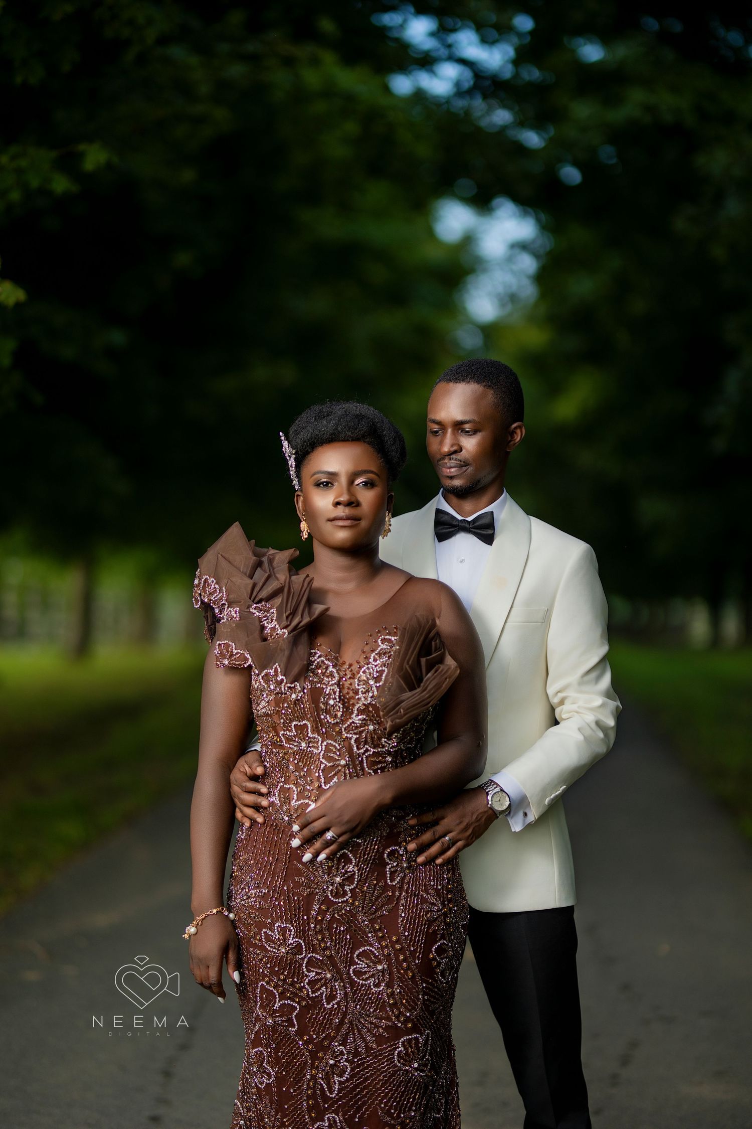 Romantic portrait of a couple in formal attire on a tree-lined path.