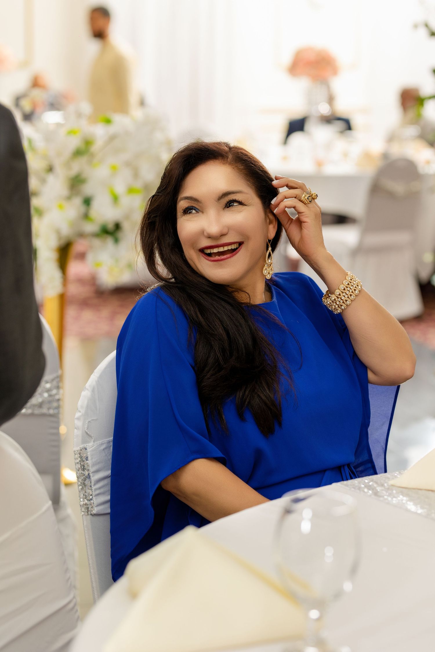 Wedding guest in royal blue cape-style dress smiles during reception celebration.