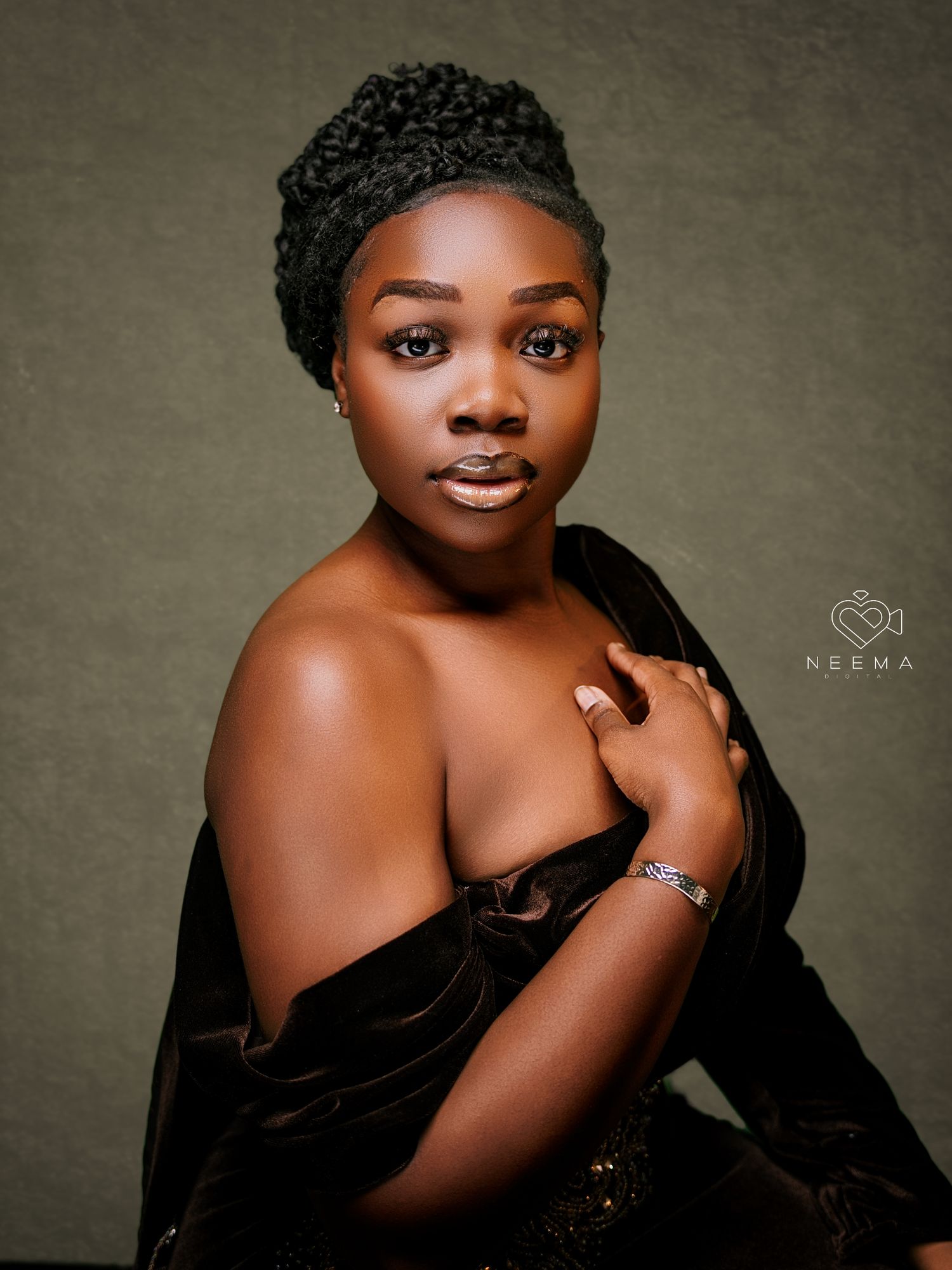 Studio beauty portrait with soft lighting featuring off-shoulder black dress and textured updo.
