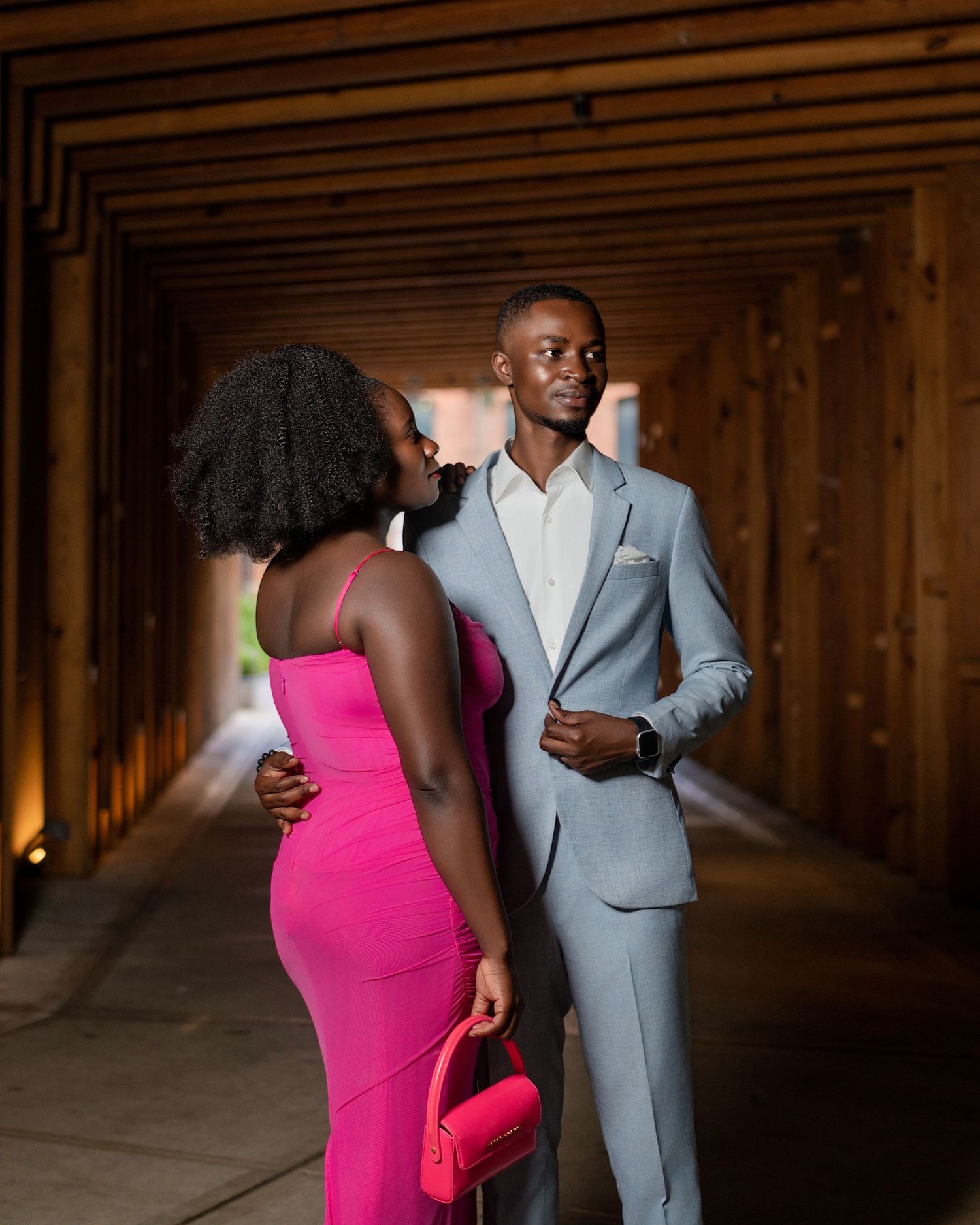 Fashionable couple in contrasting pink and grey outfits posing in wooden corridor.