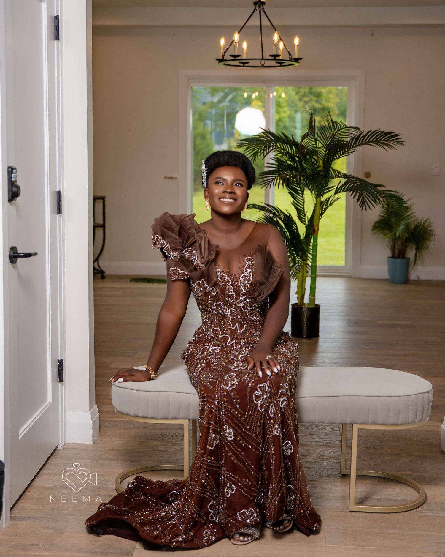 Person in sparkly brown formal gown posing in elegant room with chandelier.