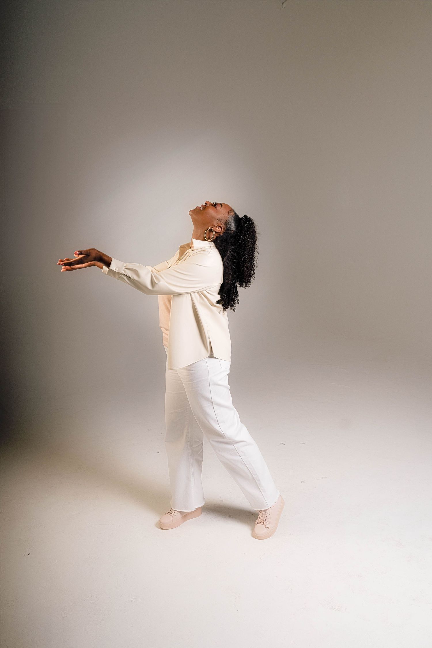 Figure in flowing white outfit dances expressively against neutral backdrop with arms outstretched.