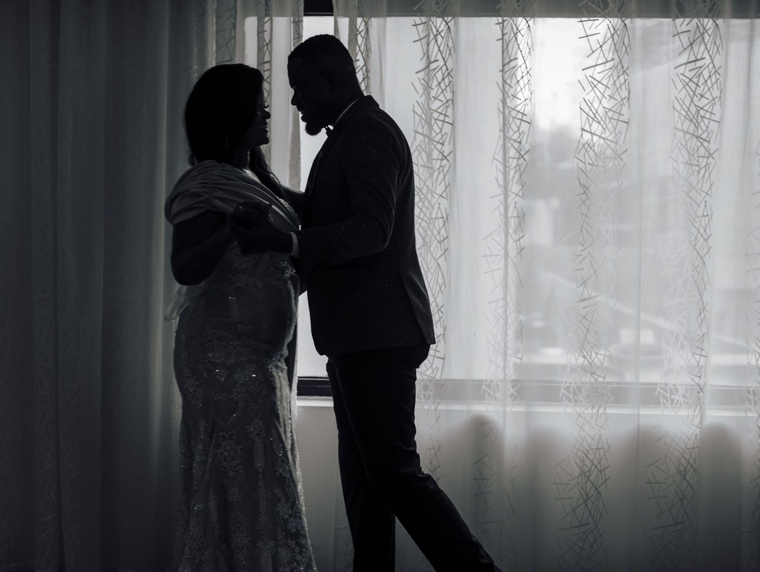 Romantic silhouette of a couple embracing against a window with lace curtains.